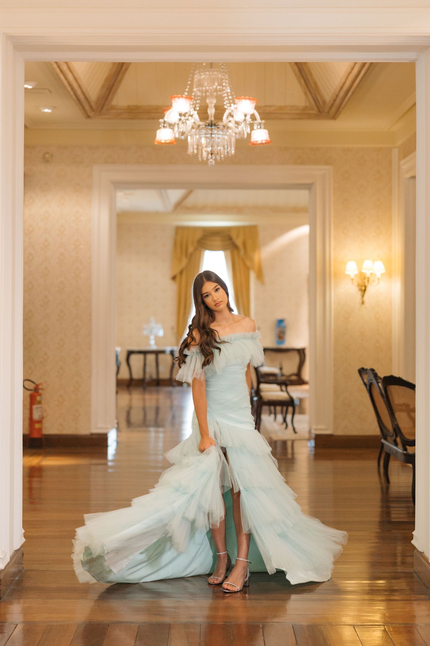 Ethereal light blue off-shoulder gown captured in elegant ballroom setting with crystal chandelier.