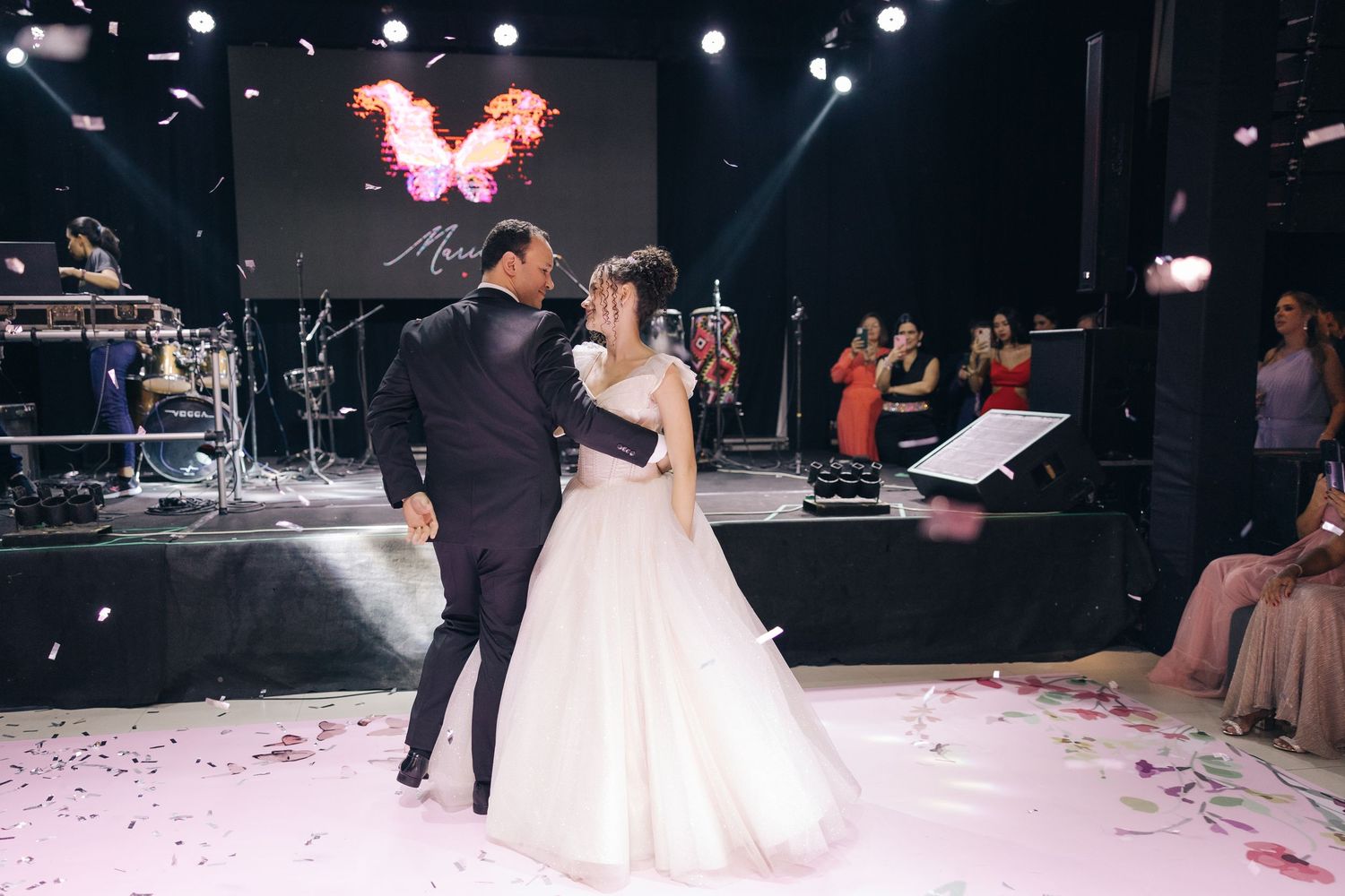 Newlyweds share romantic dance moment surrounded by confetti and stage lighting.