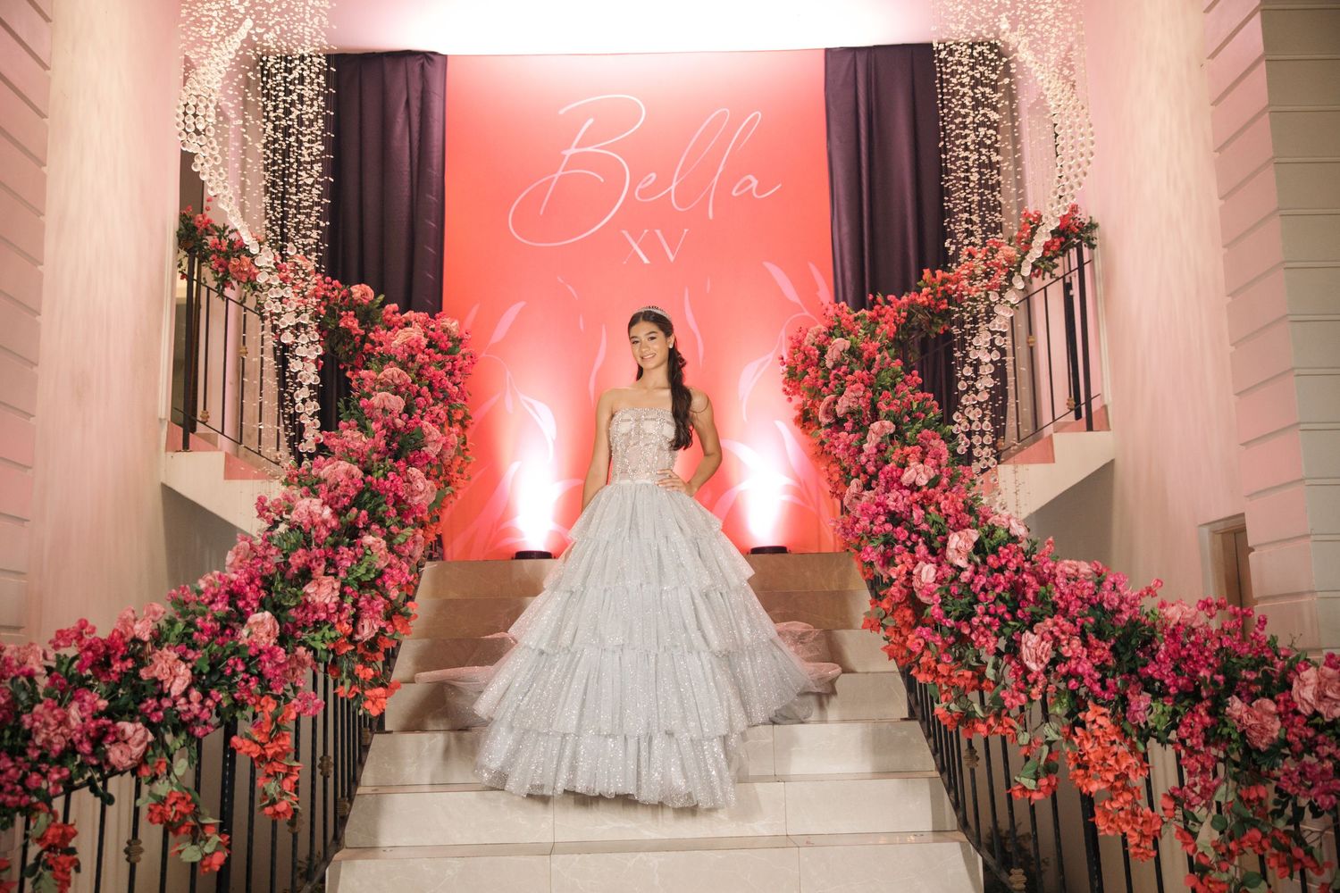 A grand entrance staircase decorated with pink floral arrangements and illuminated backdrop for a formal celebration.