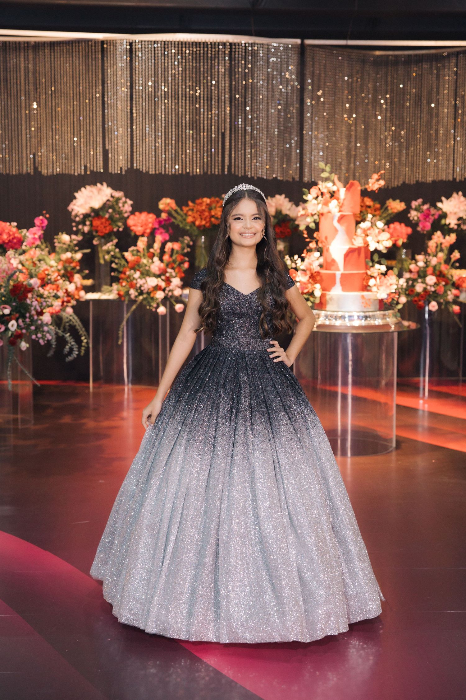A black and silver ombré ball gown displayed against floral decorations and string lights.