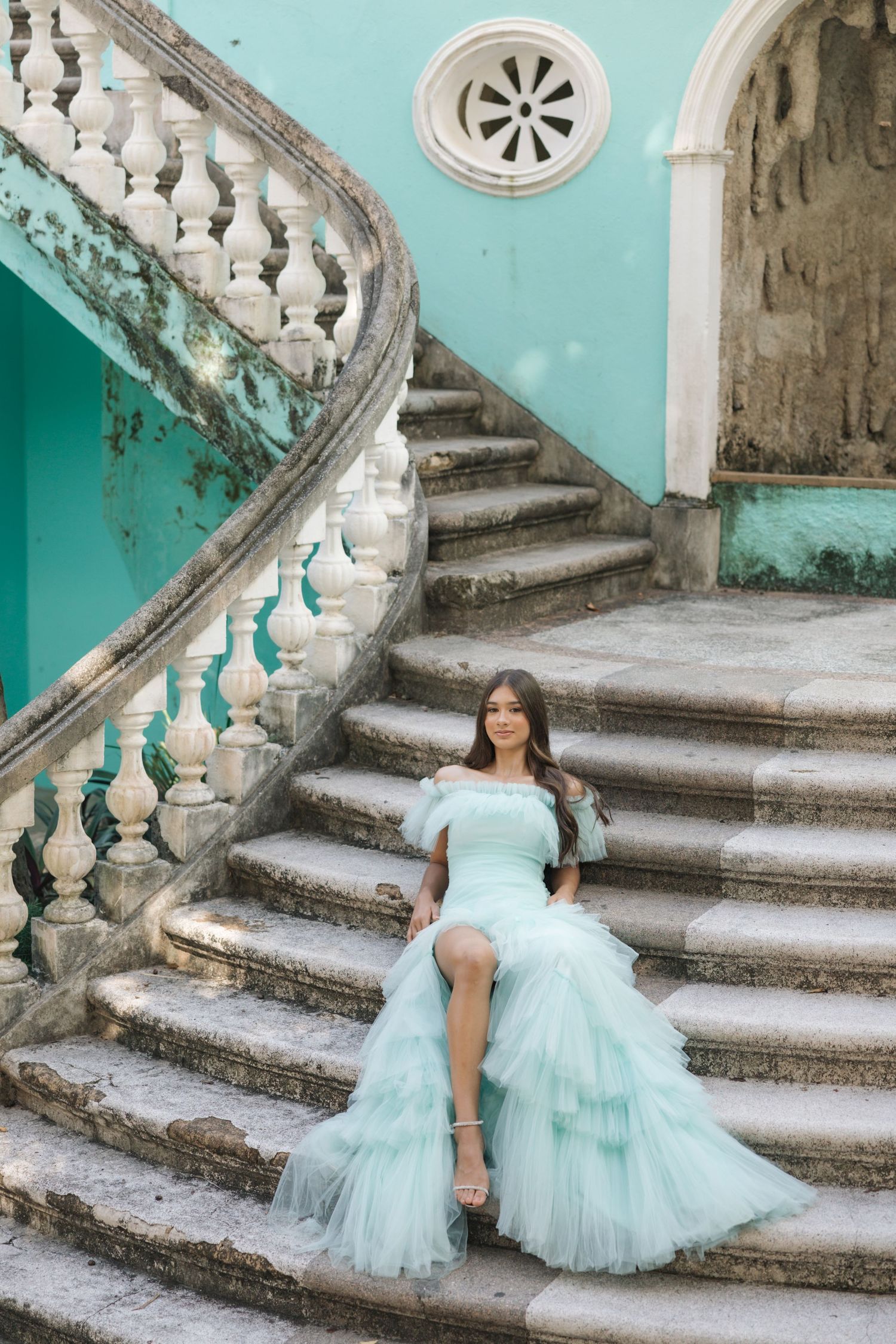Seafoam blue tulle gown showcased on historic curved staircase with ornate white balustrades and turquoise walls.