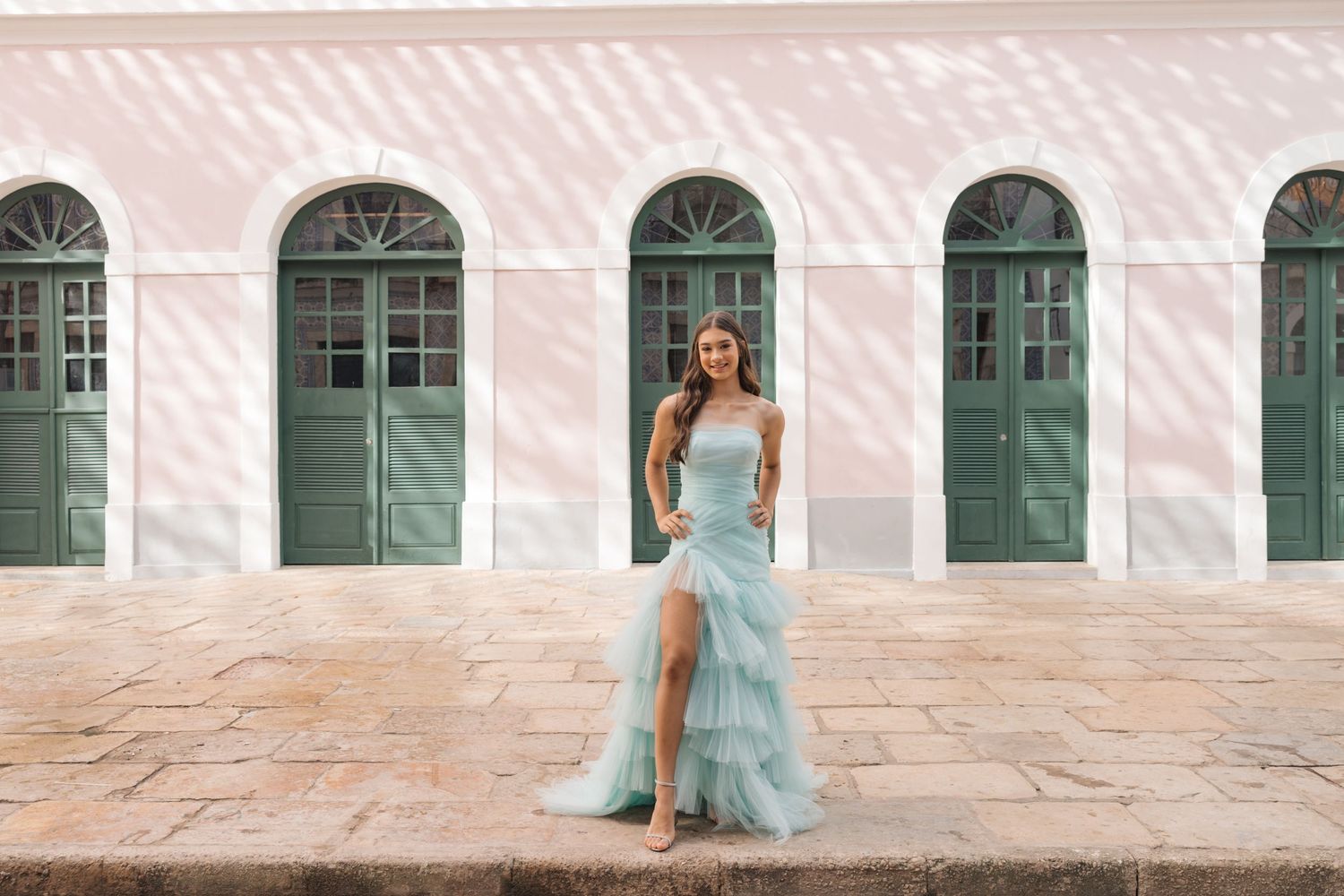 Elegant light blue gown with slit photographed against pink wall with green doors in historic architecture setting.