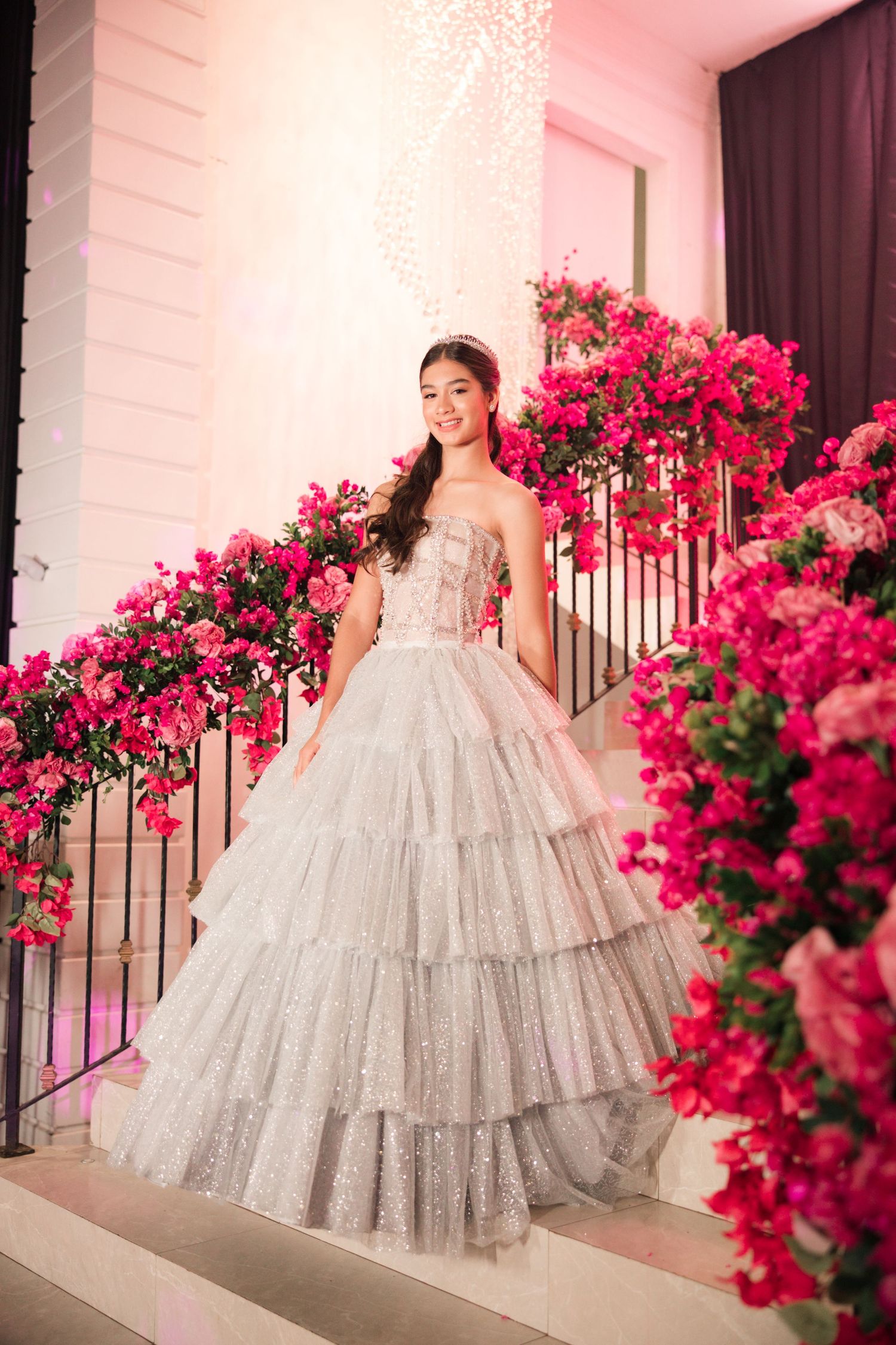 A layered tulle ballgown sparkles against a backdrop of vibrant pink bougainvillea flowers and white columns.