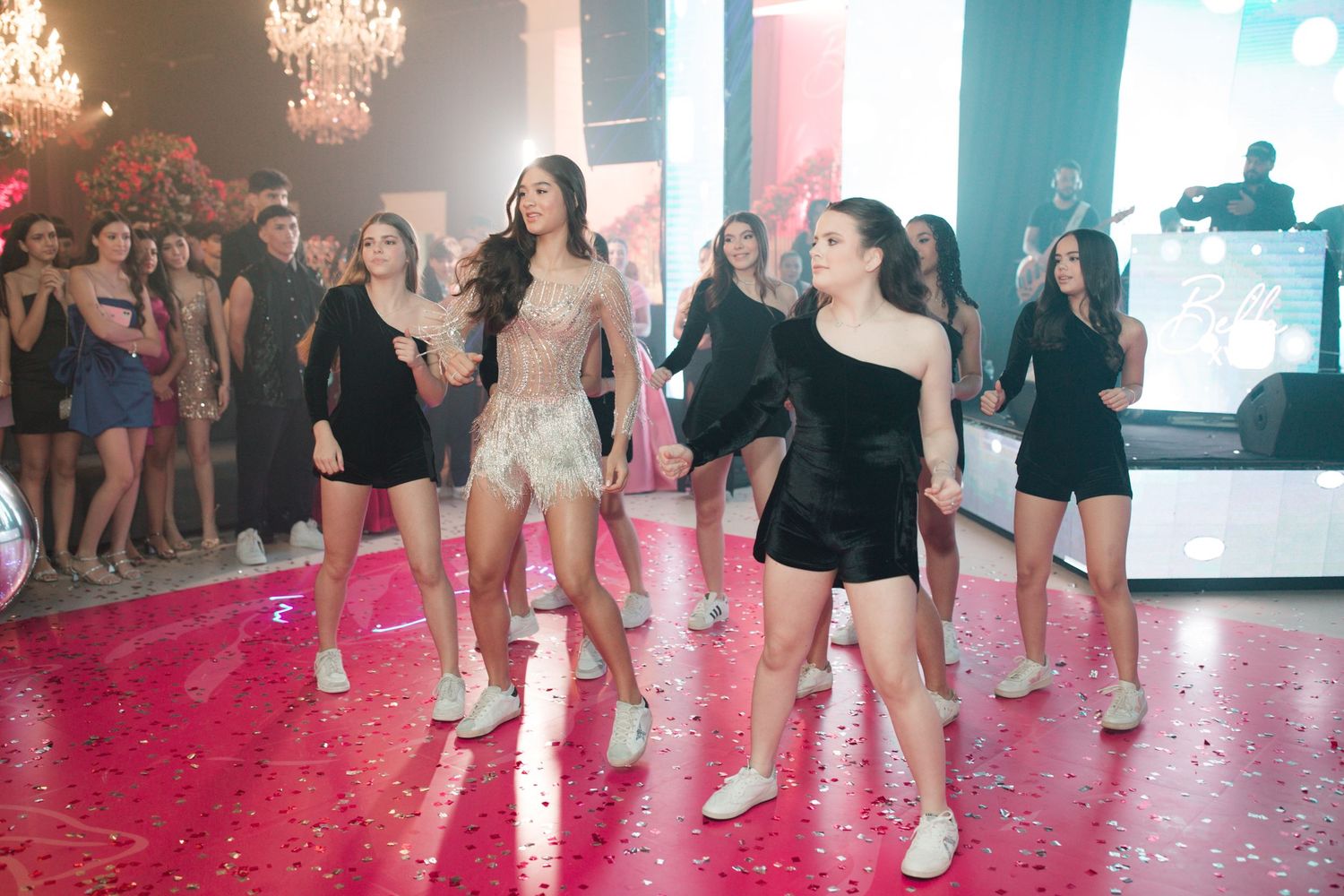 Party guests dancing on a pink-lit dance floor during a festive quinceañera celebration.
