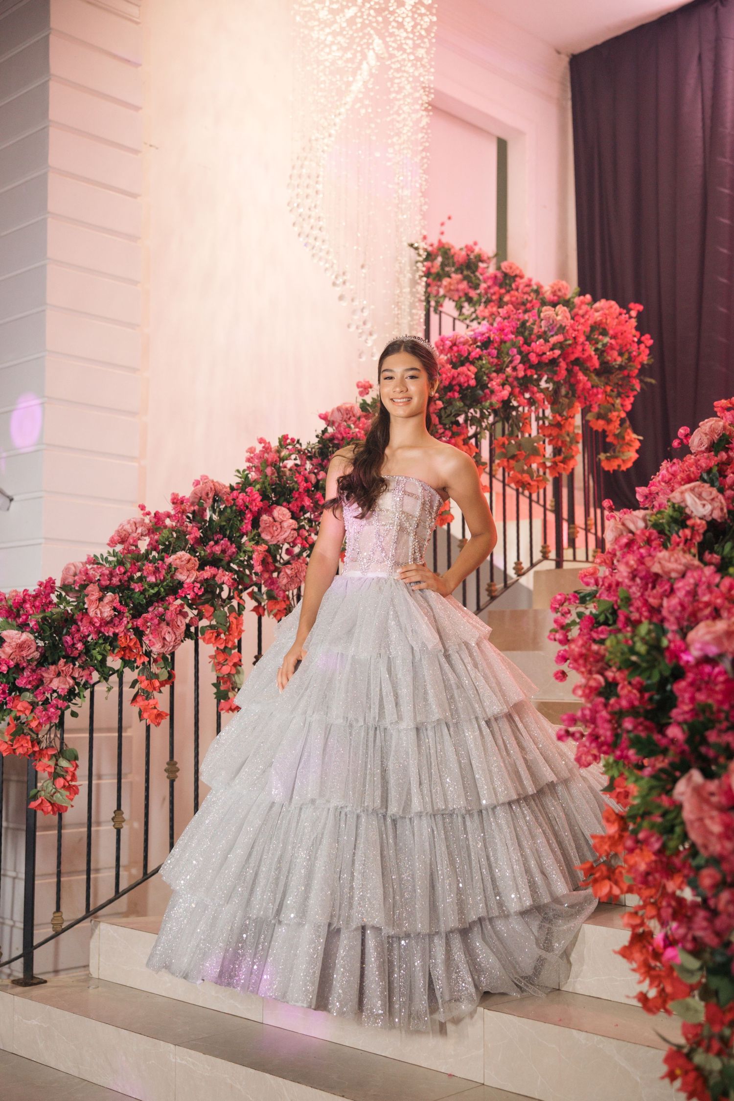 A sparkly silver ballgown dress photographed on elegant stairs decorated with vibrant pink floral arrangements.