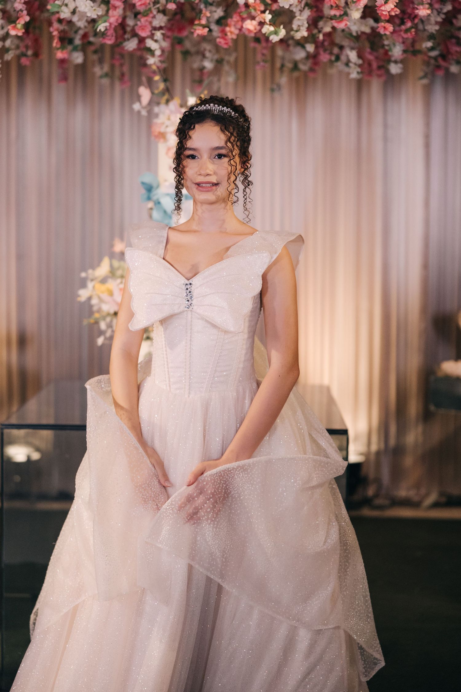White princess ballgown with corset bodice surrounded by pink floral decorations.