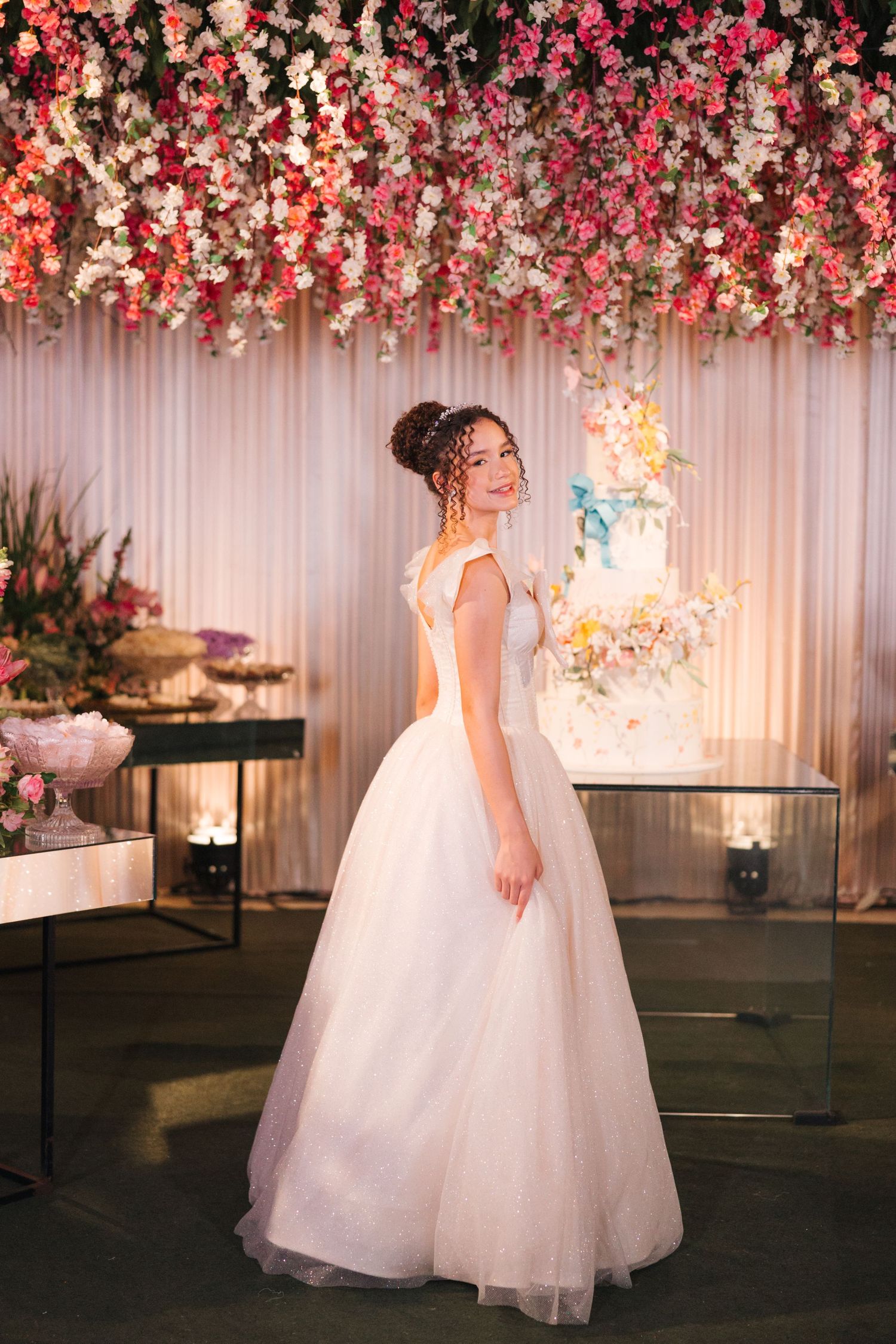 Elegant wedding gown showcased beneath stunning floral canopy with blush and pink blooms in luxurious reception setting.