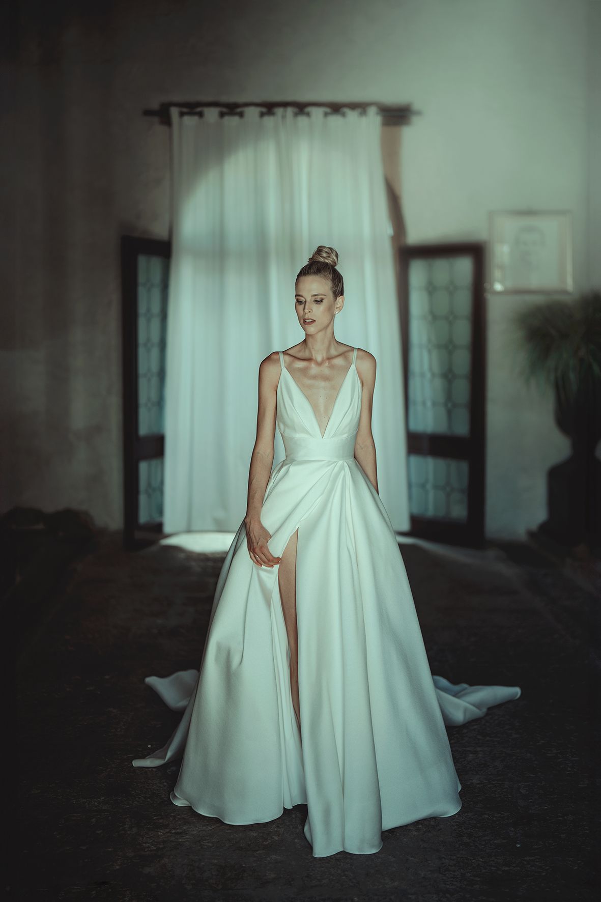 Modern bride poses in minimalist white wedding gown with dramatic side slit in moody lighting.