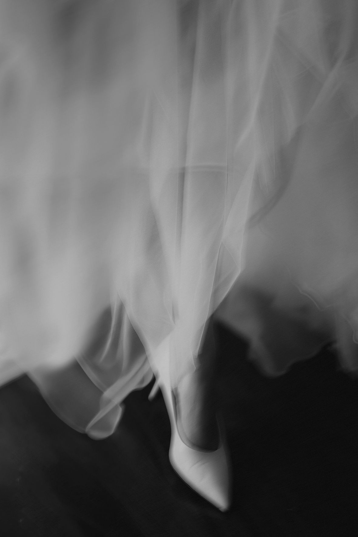 Ethereal black and white photo of wedding dress fabric flowing around bride's shoes.
