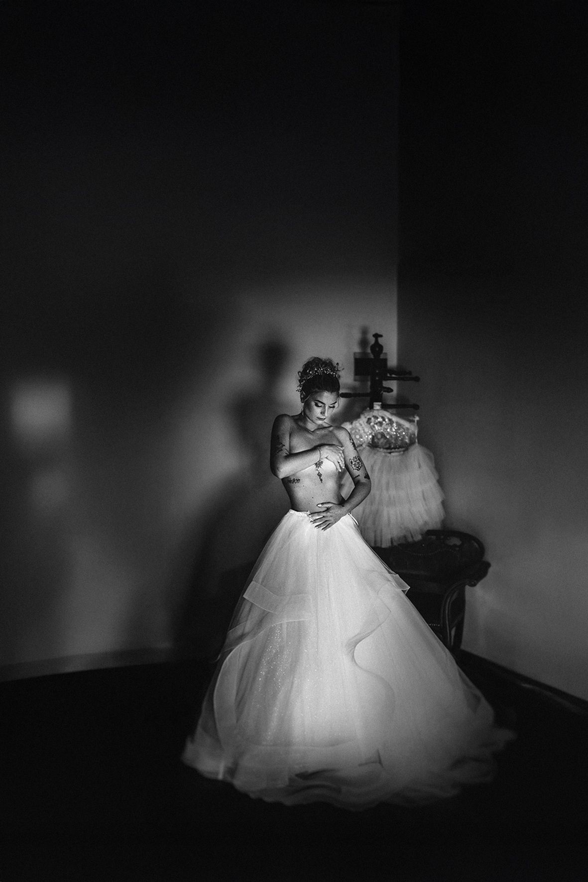 Elegant bride in a flowing white tulle wedding gown stands in a dramatic black and white photo.
