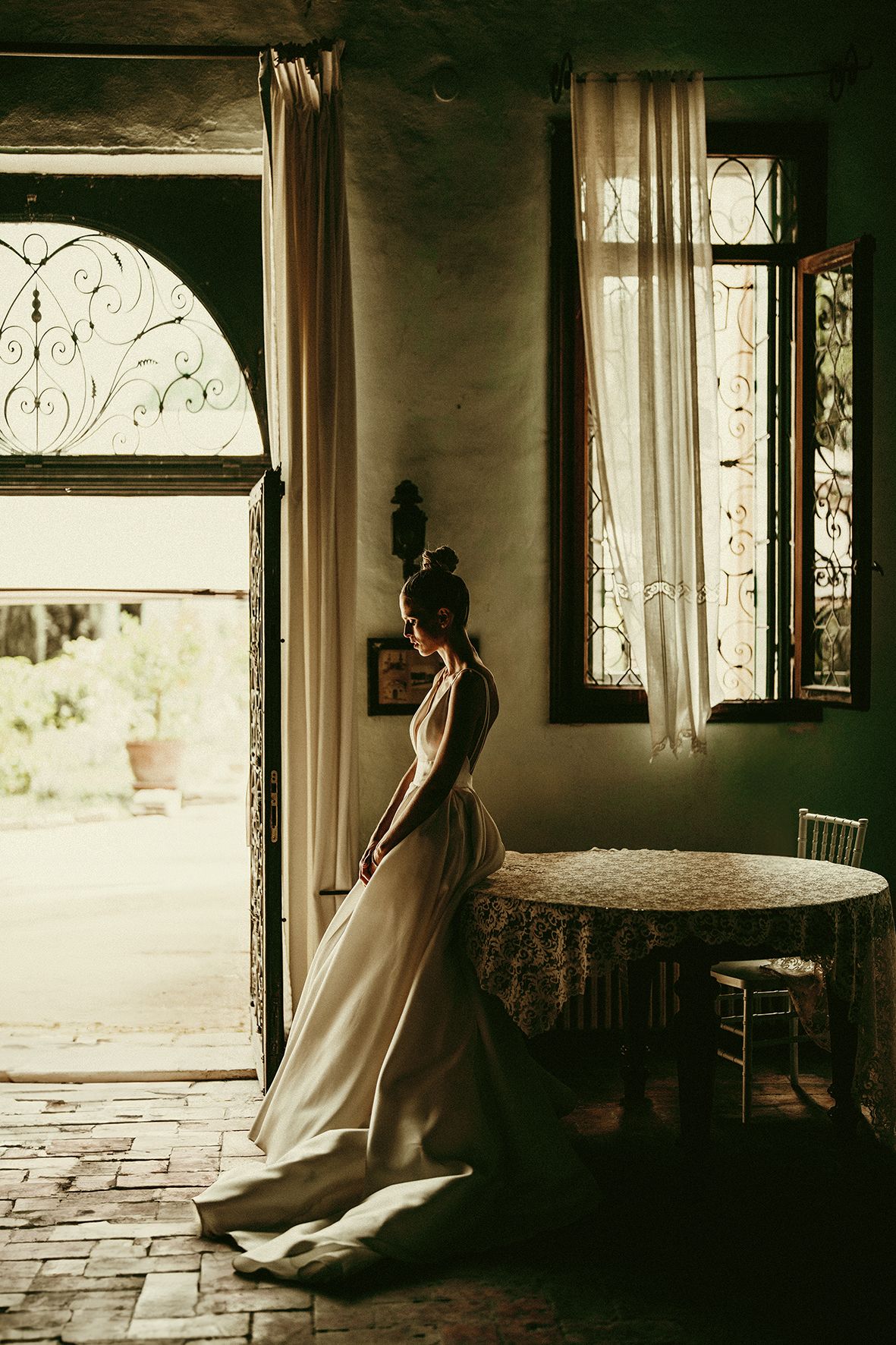 Silhouette of bride in flowing dress stands by arched doorway in vintage interior.