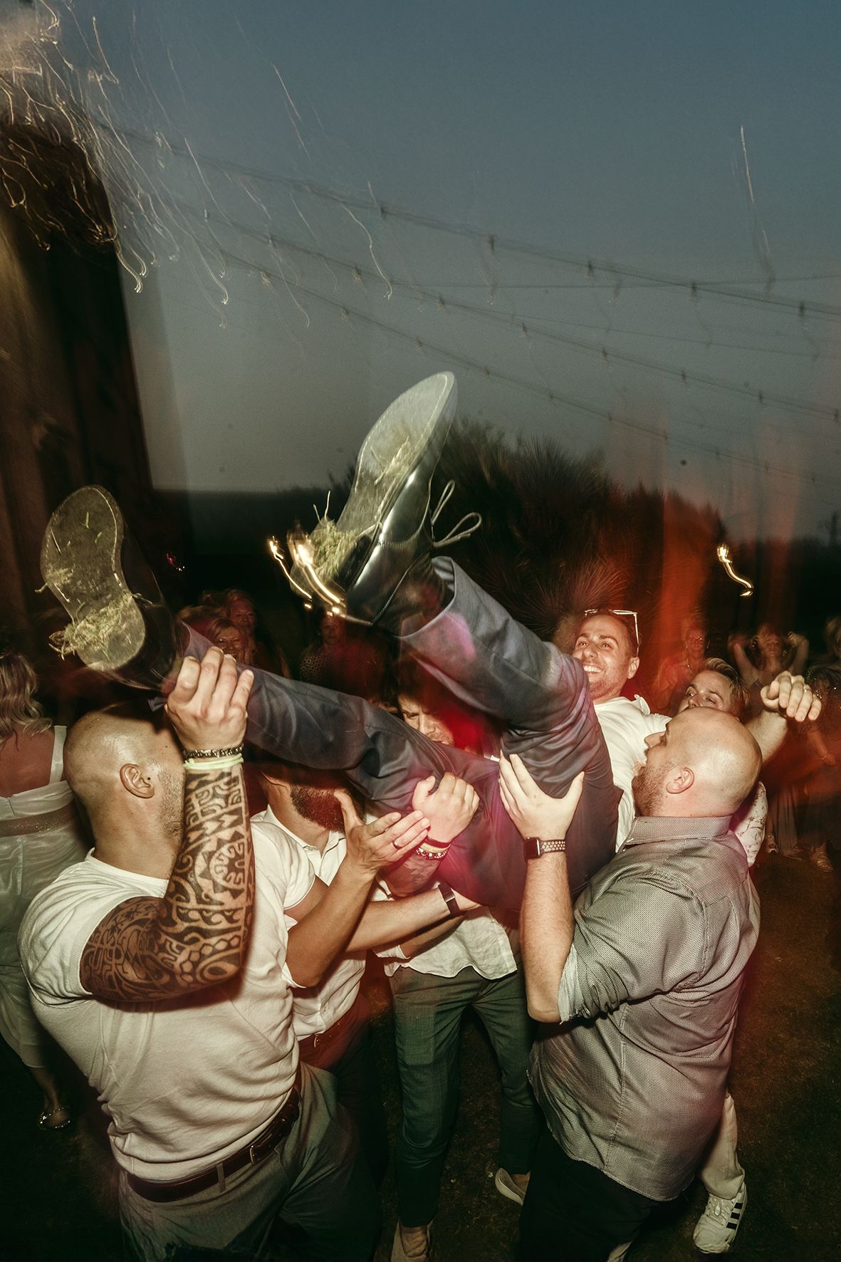 People dancing and jumping energetically at a crowded party with drinks spilling through the air.