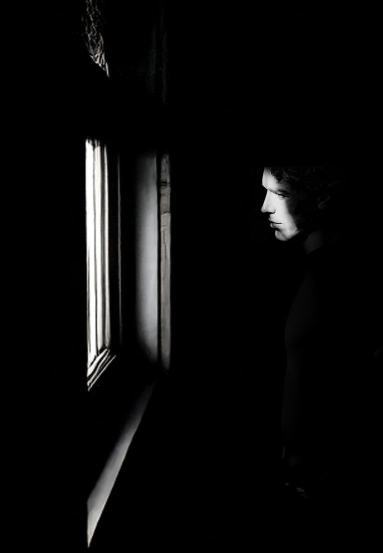 A dramatic black and white silhouette of a person gazing contemplatively through a window in darkness.