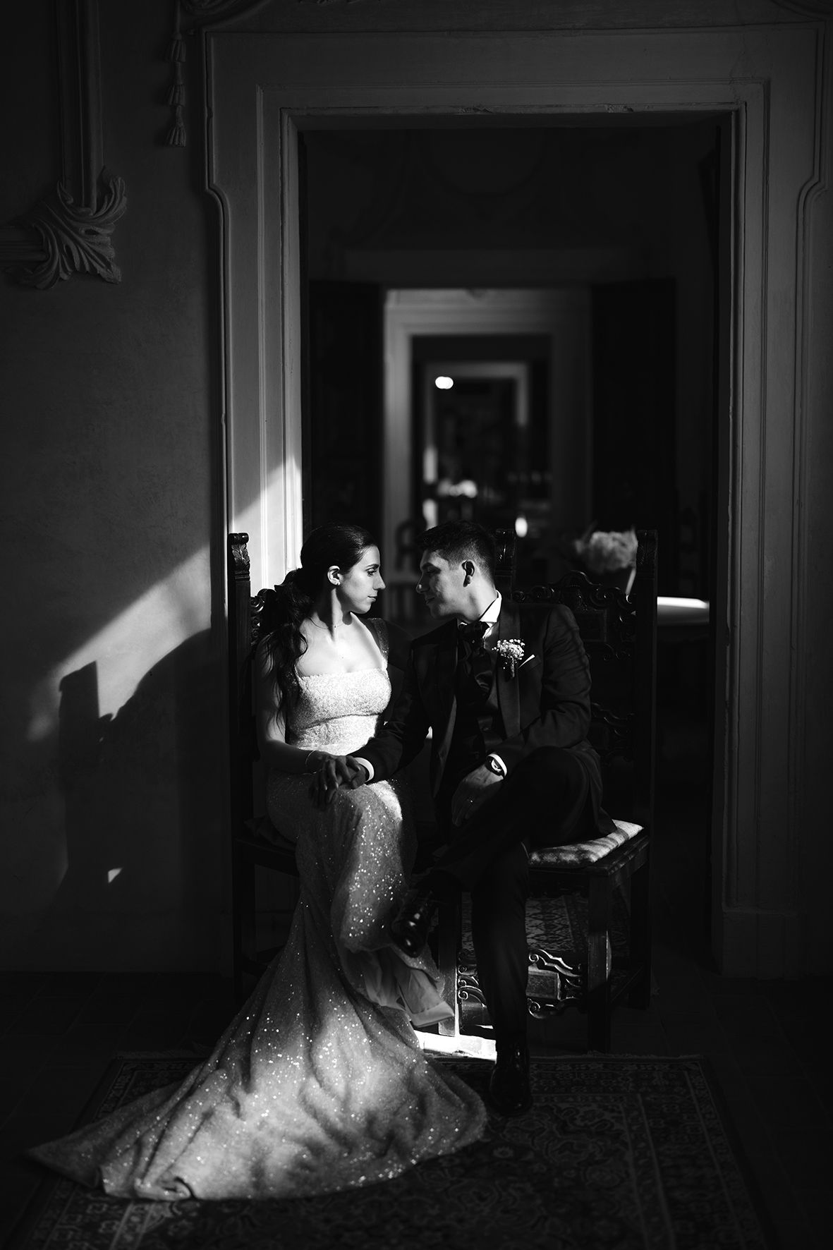 A couple shares an intimate moment in a darkly lit hallway during a wedding, captured in black and white photography.