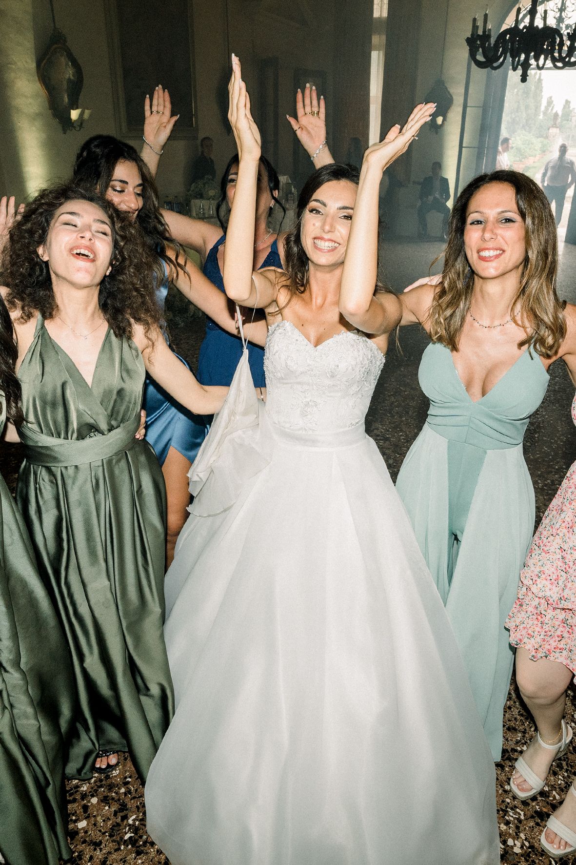 Wedding party celebrating and dancing together with their hands in the air at a reception venue.