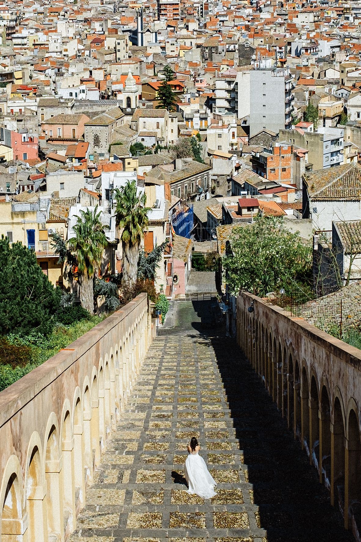 Historic stone wall with arches overlooks dense terracotta rooftops and urban landscape of Mediterranean city.