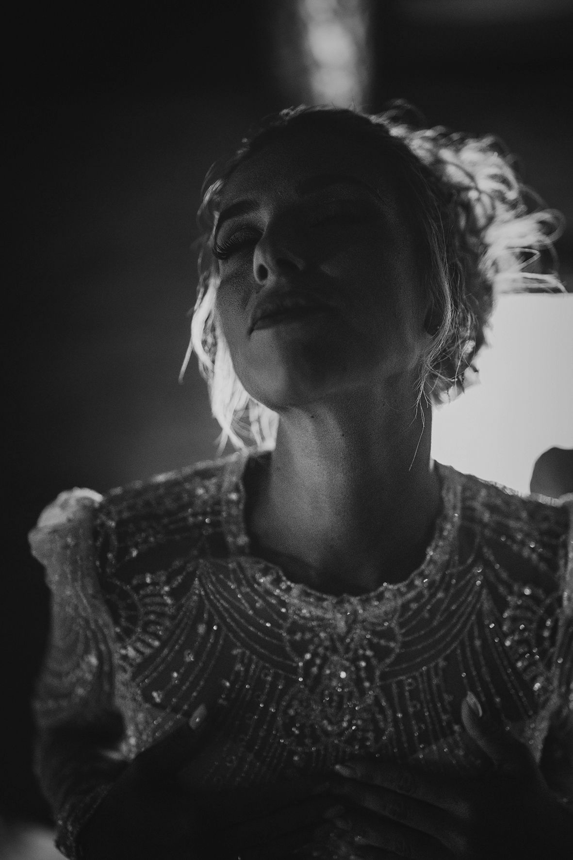 Dramatic black and white portrait of figure in beaded evening dress with moody lighting.