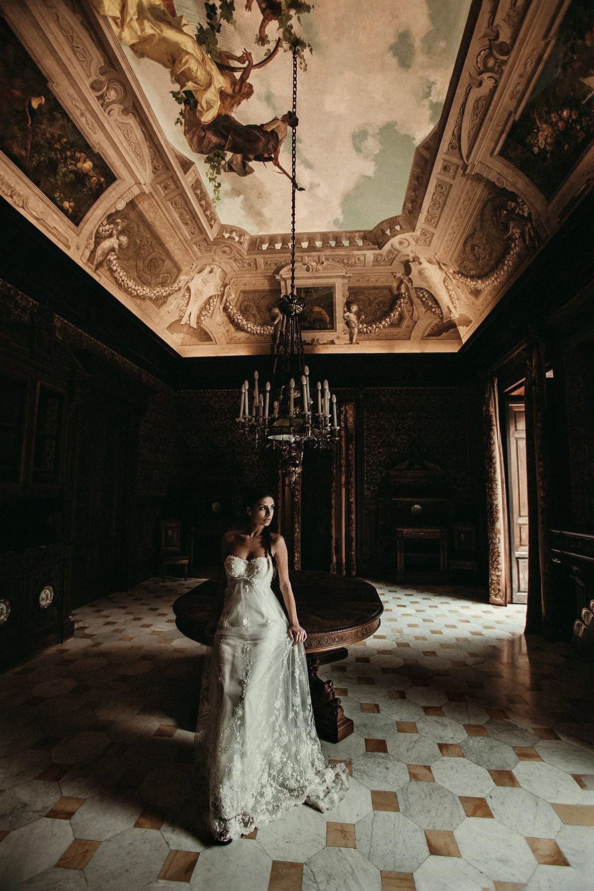 Dramatic bridal portrait in an opulent ballroom with ornate ceiling frescoes and chandelier.