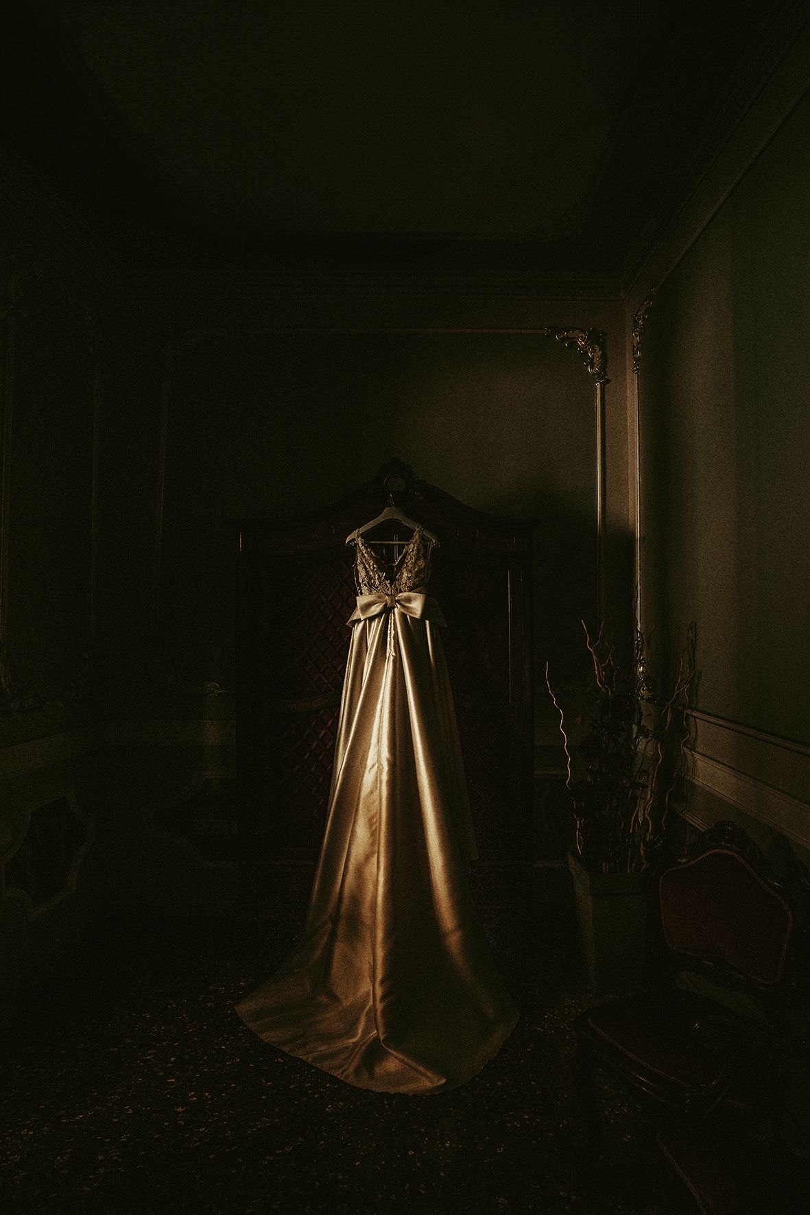 Wedding dress on display in dark moody room illuminated by single light source.
