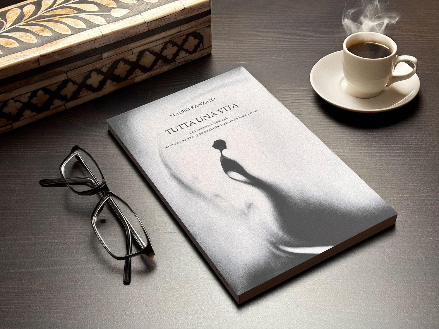 A stylish still life with a book, reading glasses, and coffee cup on a dark wooden desk.