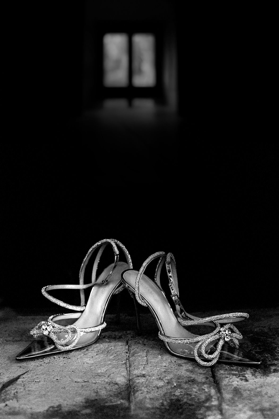 Black and white image of elegant bridal shoes with decorative details on stone surface.