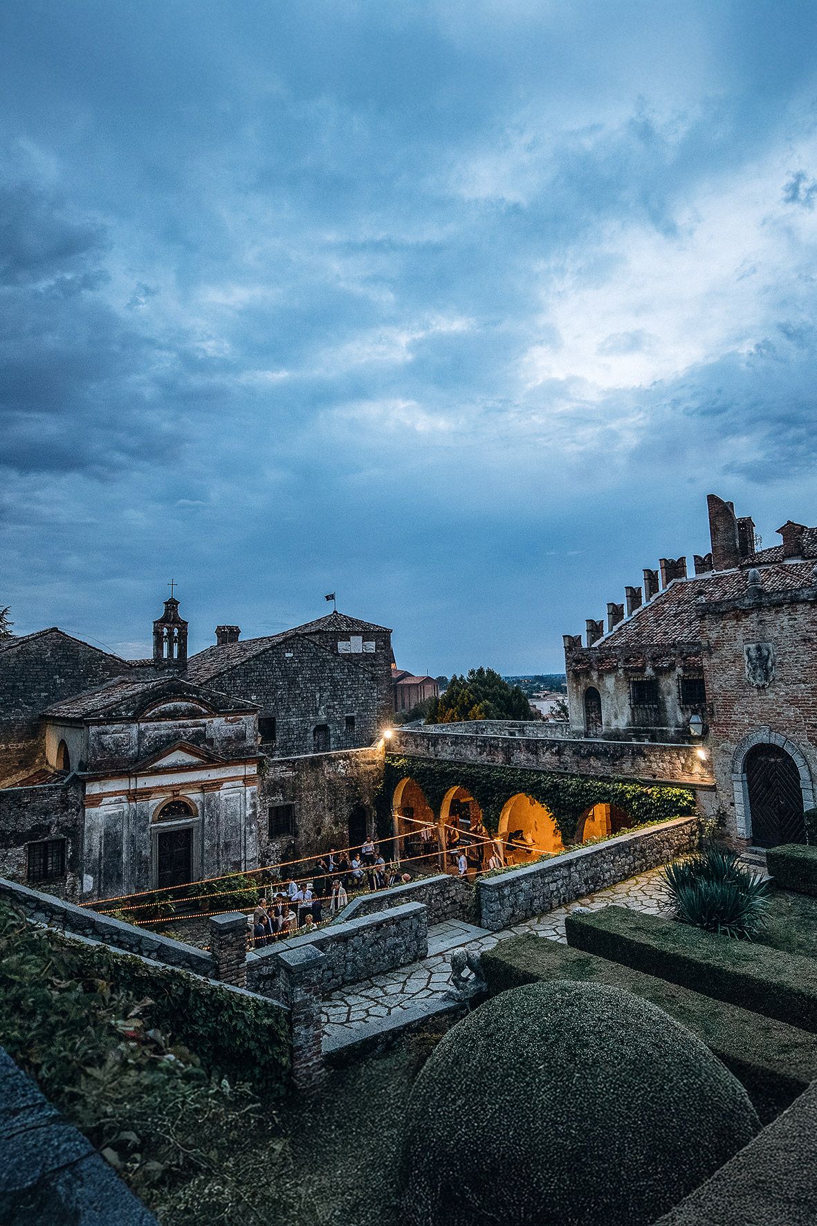 Historic stone fortress with illuminated arches and terraces at dusk under dramatic blue cloudy skies.