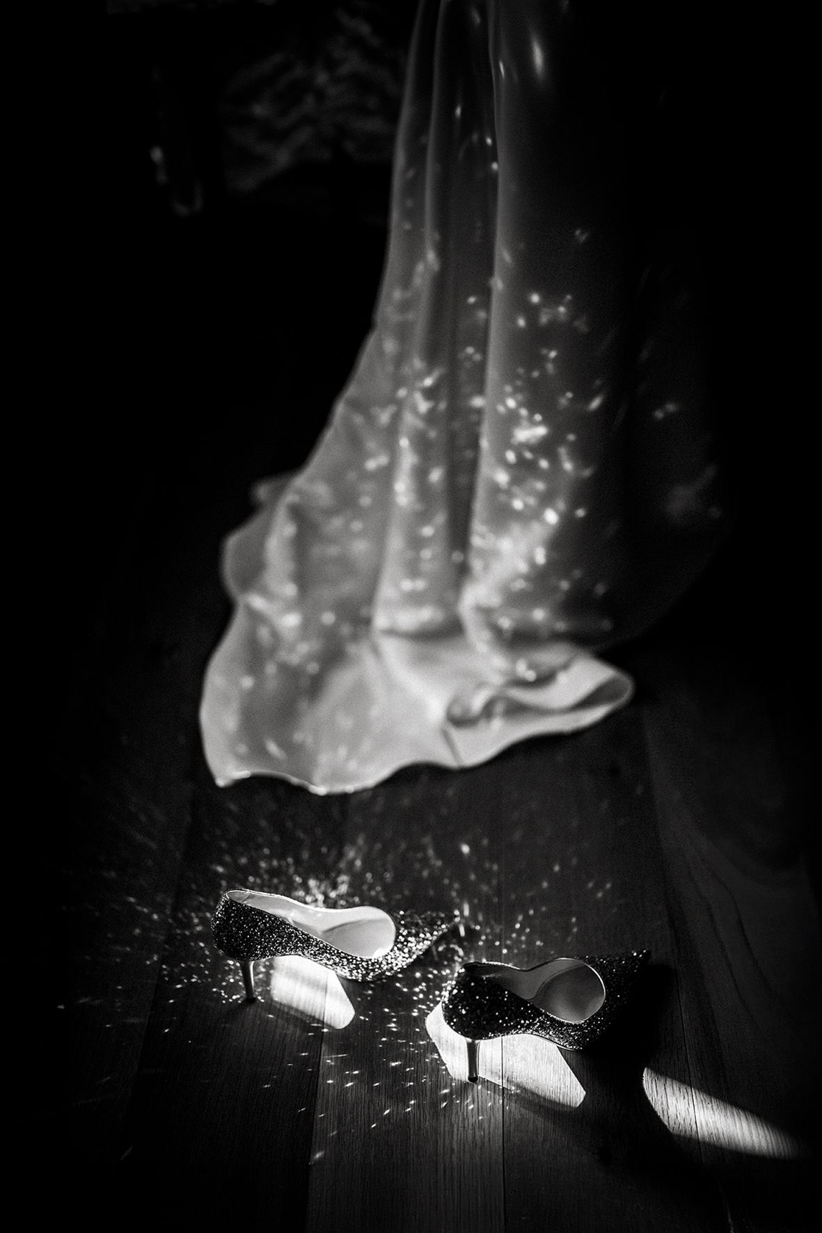 Wedding shoes and dress hem with sparkles in dramatic black and white photography.