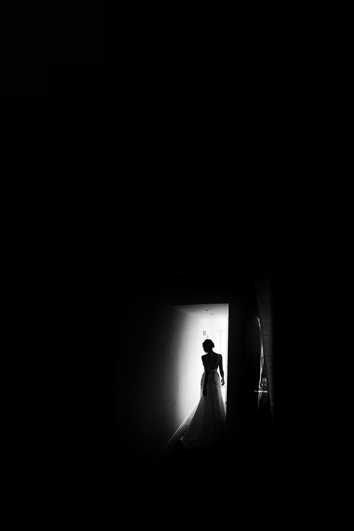 A silhouetted figure in a wedding dress stands dramatically in a bright doorway against dark surroundings.