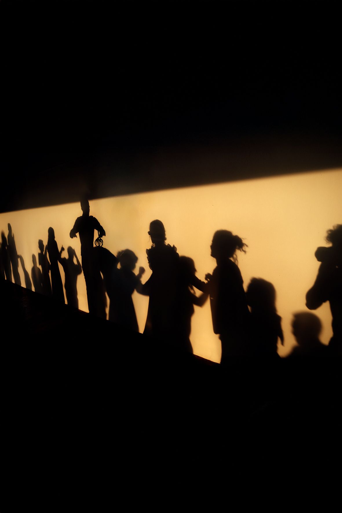 Silhouettes of people dancing and raising hands against a warm golden sunset backdrop create a lively party atmosphere.