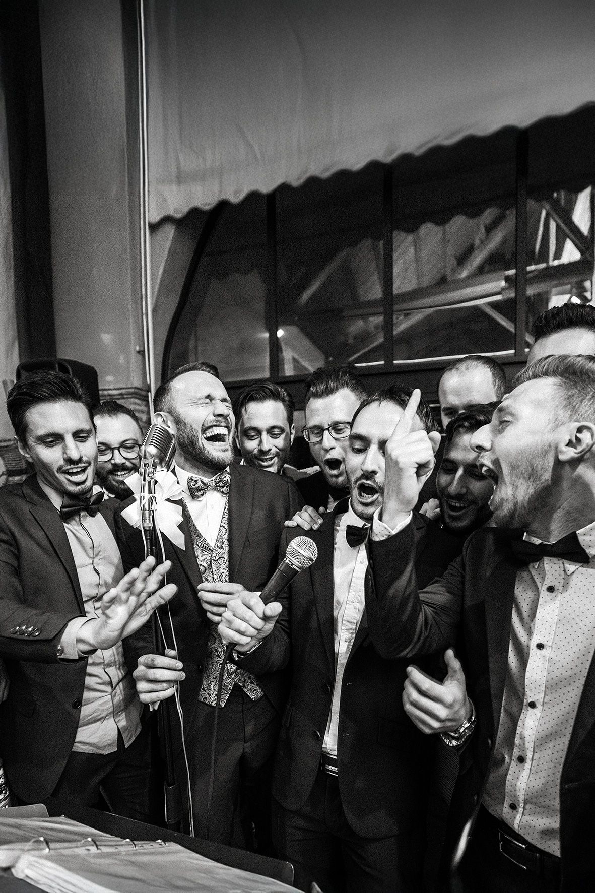 Group in formal attire passionately singing together at a celebration in black and white photography.