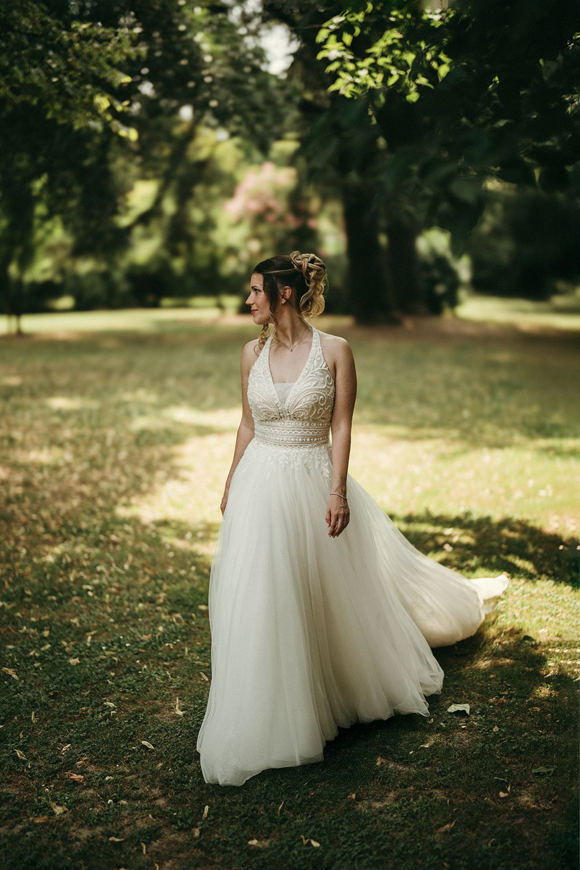 A bride in a flowing white tulle gown twirls gracefully outdoors in a sun-dappled garden setting.