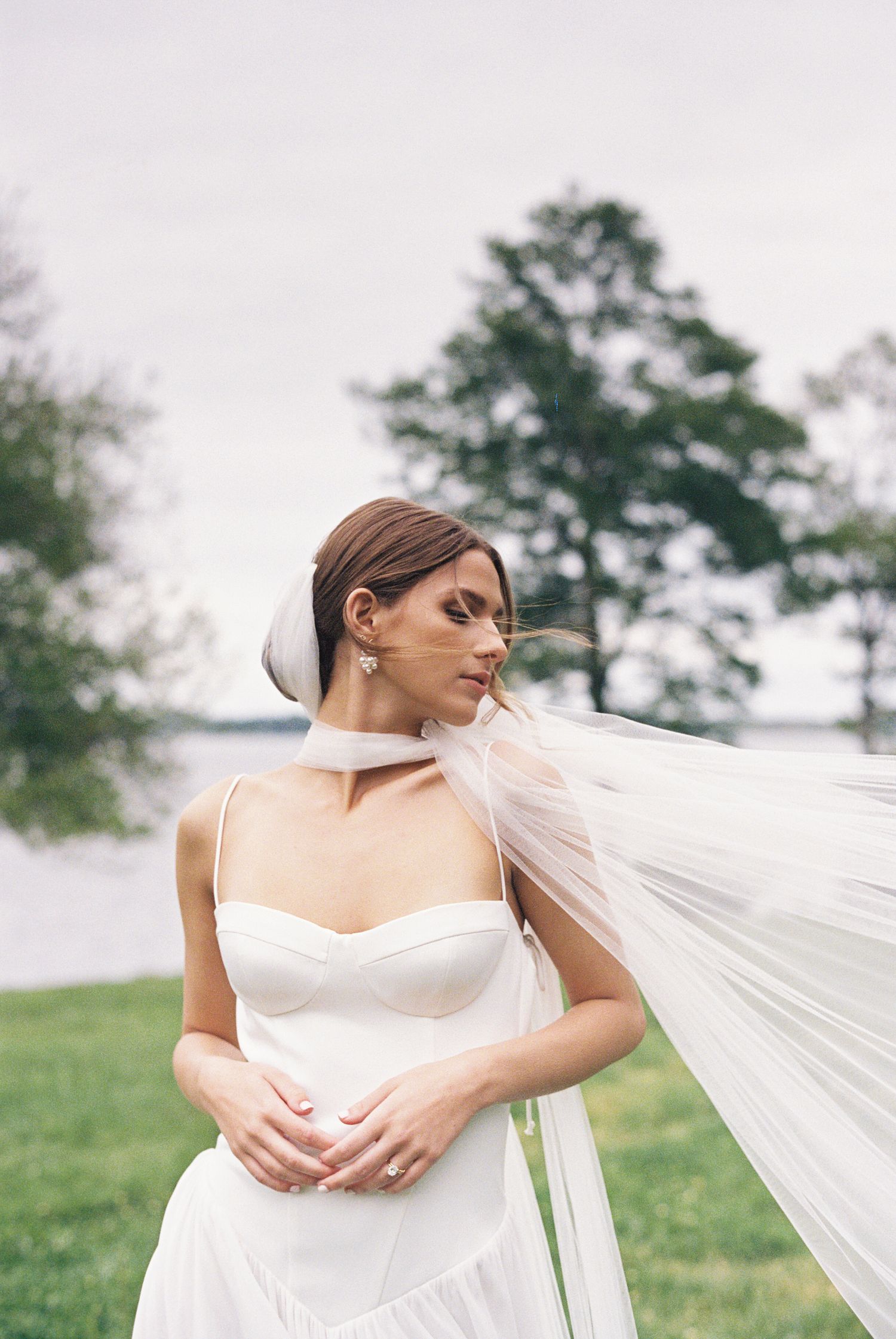 A film portrait of a bride in a white wedding dress stands in a meadow as her long veil flows gracefully in the wind. Glen Manor, RI