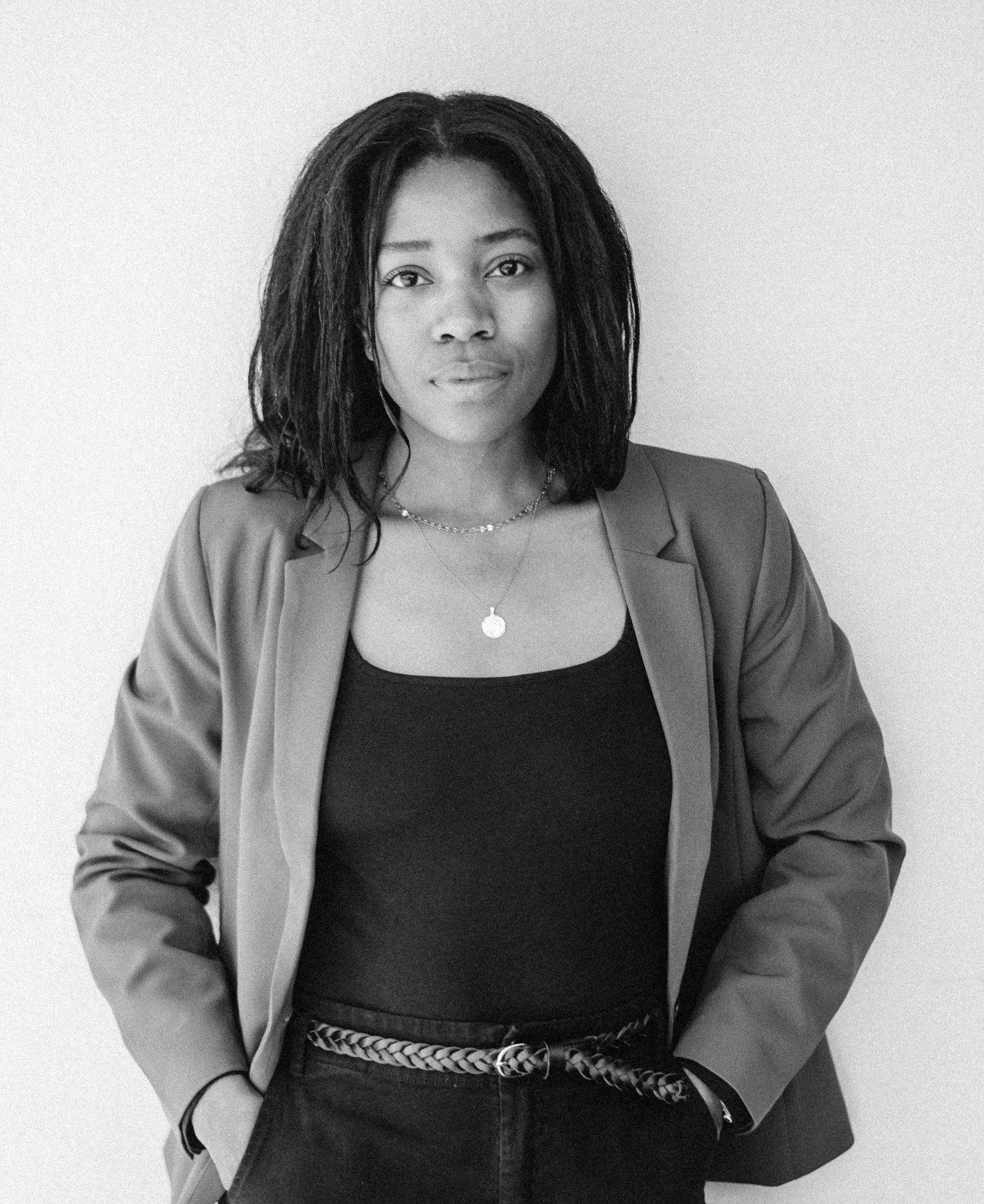 Professional studio portrait in black and white showing a person wearing a blazer and black top with braided belt.