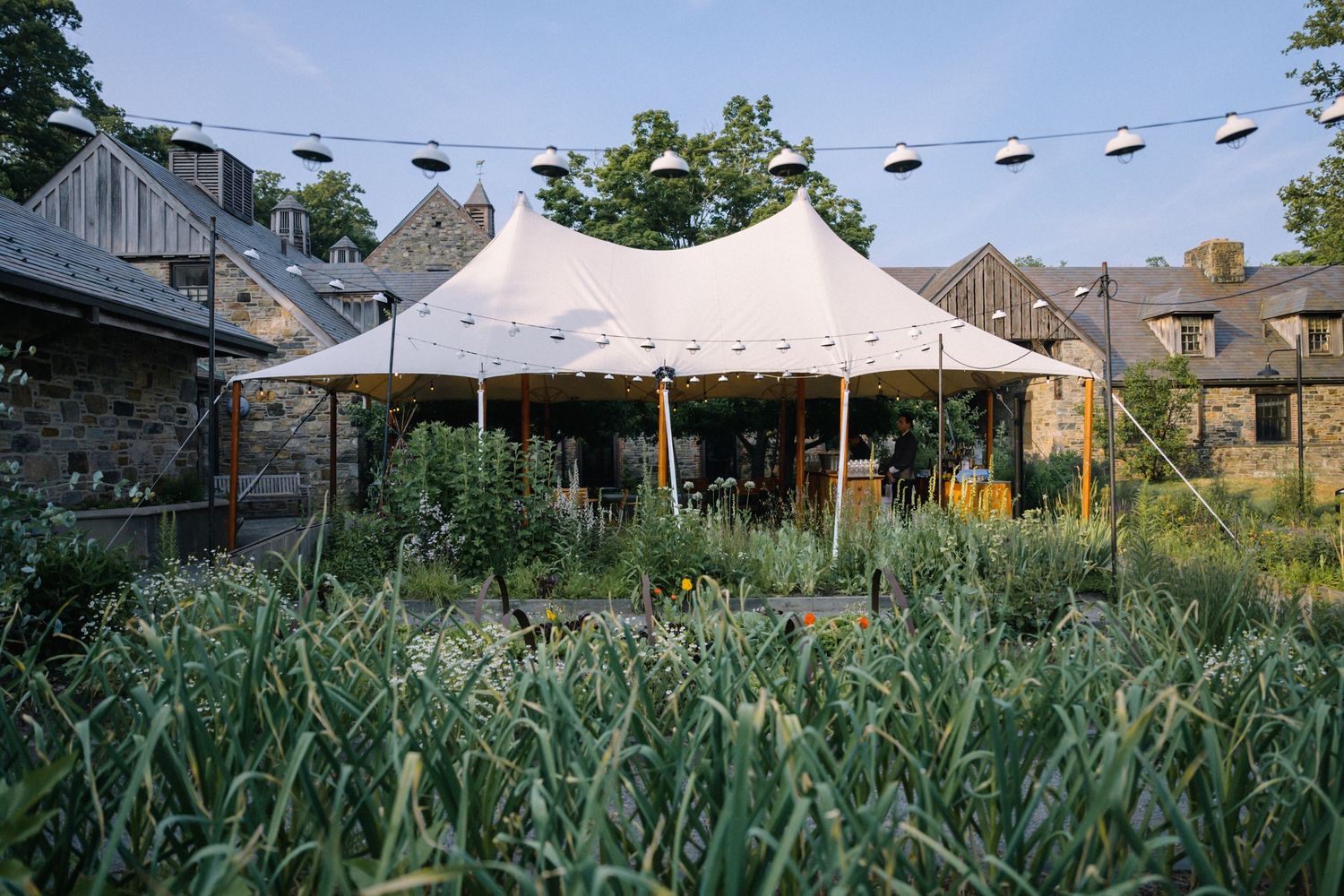 A white event tent stands in a lush garden at a Blue Hill Stone Barn wedding in New York