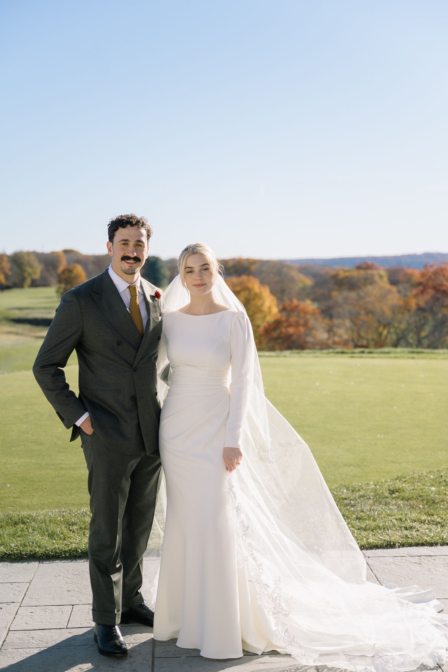 Bride and groom stand on stone patio with autumn foliage and rolling hills in background during outdoor ceremony in Connecticut.