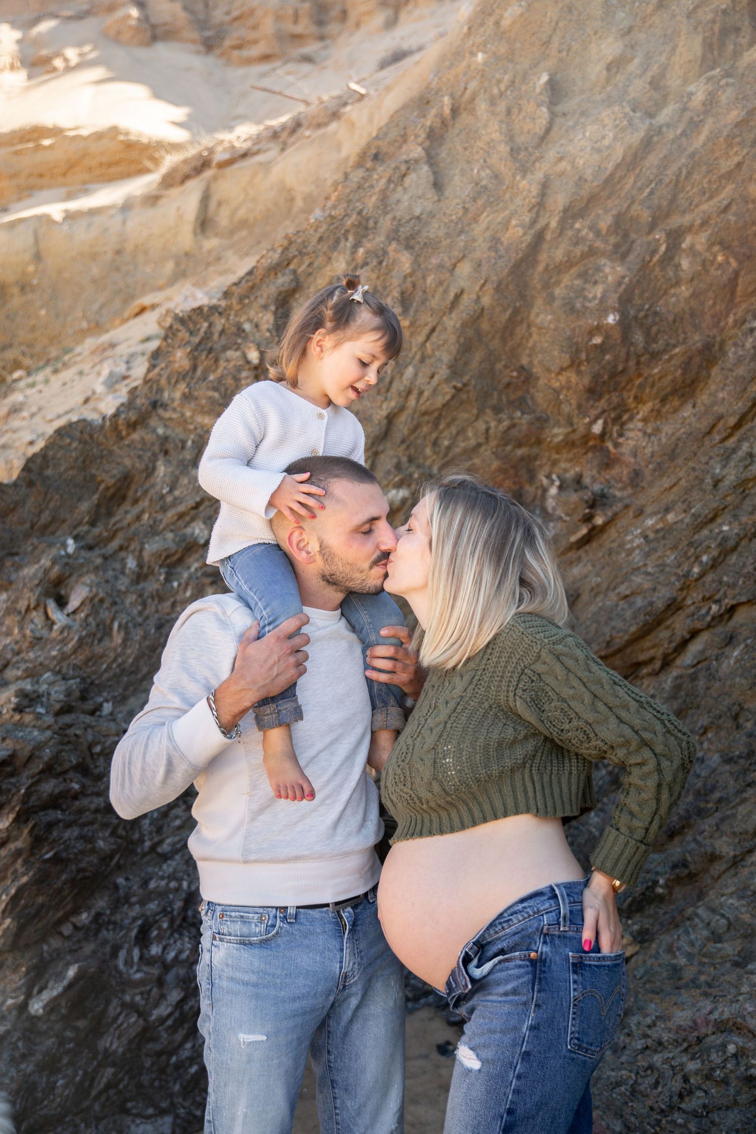 Couple et leur fille profitant d’un moment tendre à la plage avant l’arrivée du bébé.