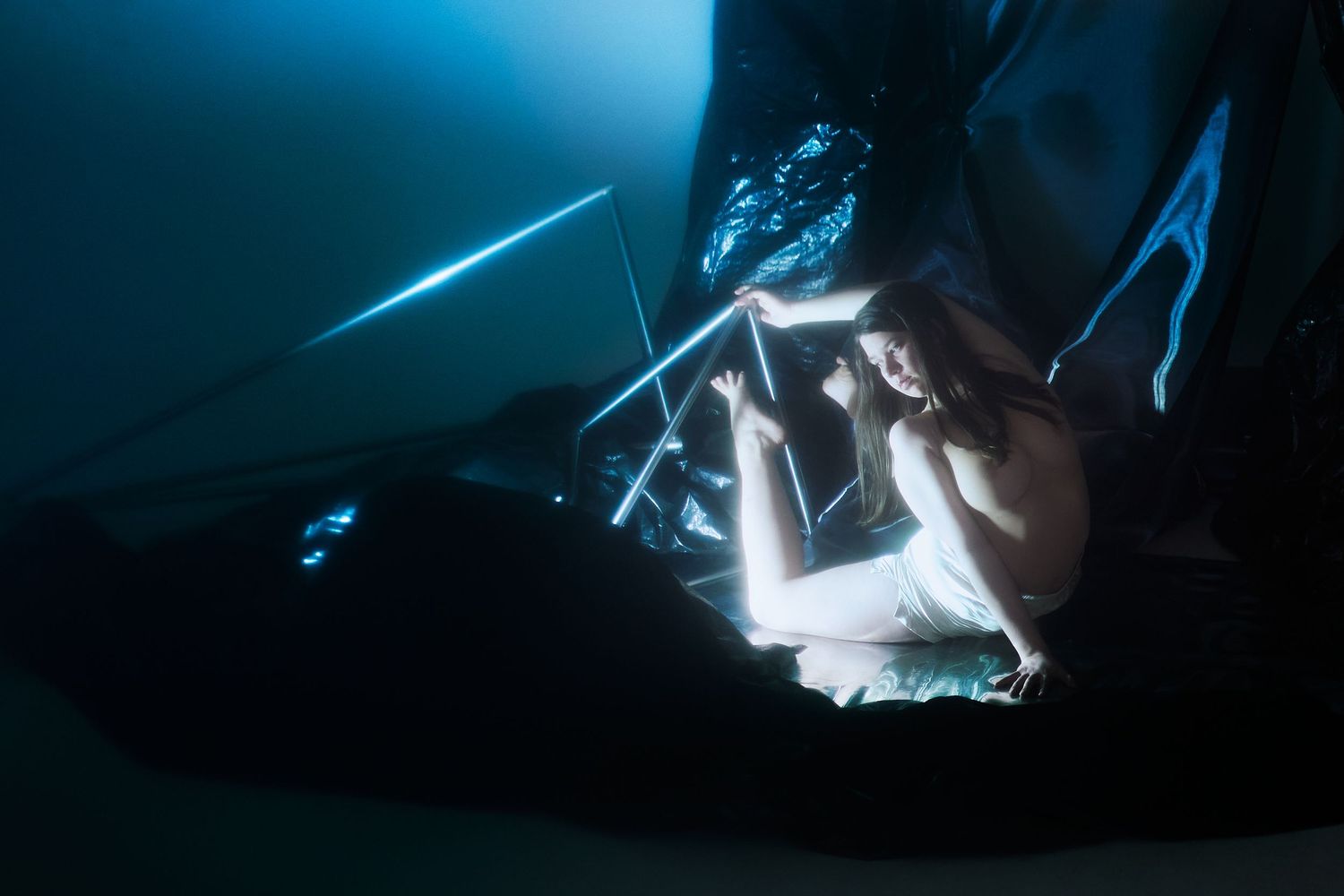 An underwater cave illuminated by shimmering blue light filters through a dark, rocky crevice beneath the ocean surface.