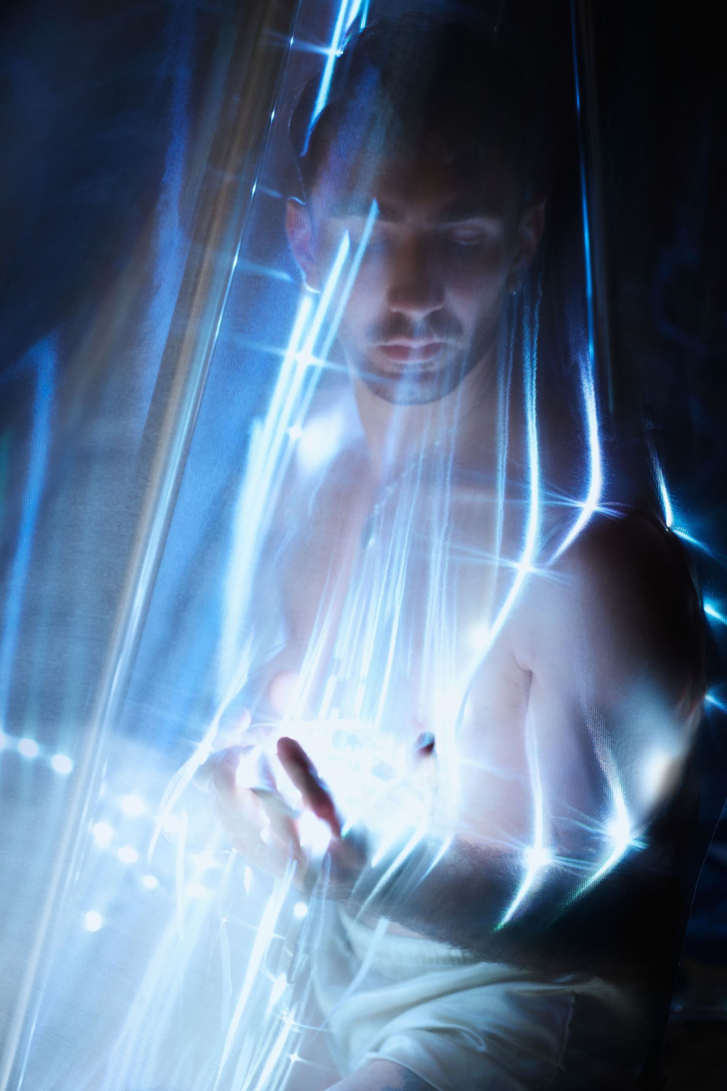 A figure emerges through ethereal blue light streaks creating a moody artistic portrait with dramatic lighting effects.