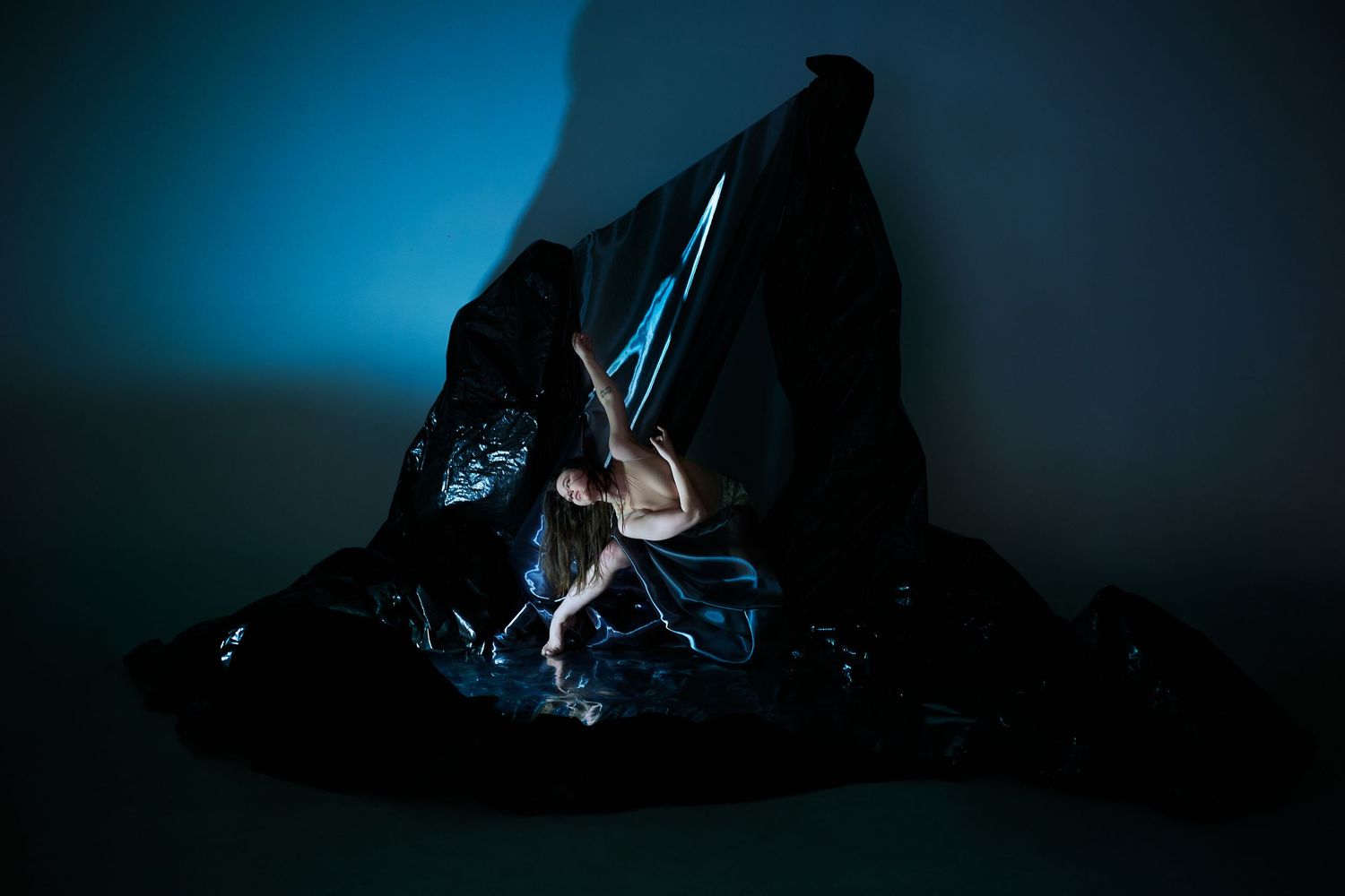 A dramatic silhouette of a climber scaling a dark rock face against a moody blue-lit background.