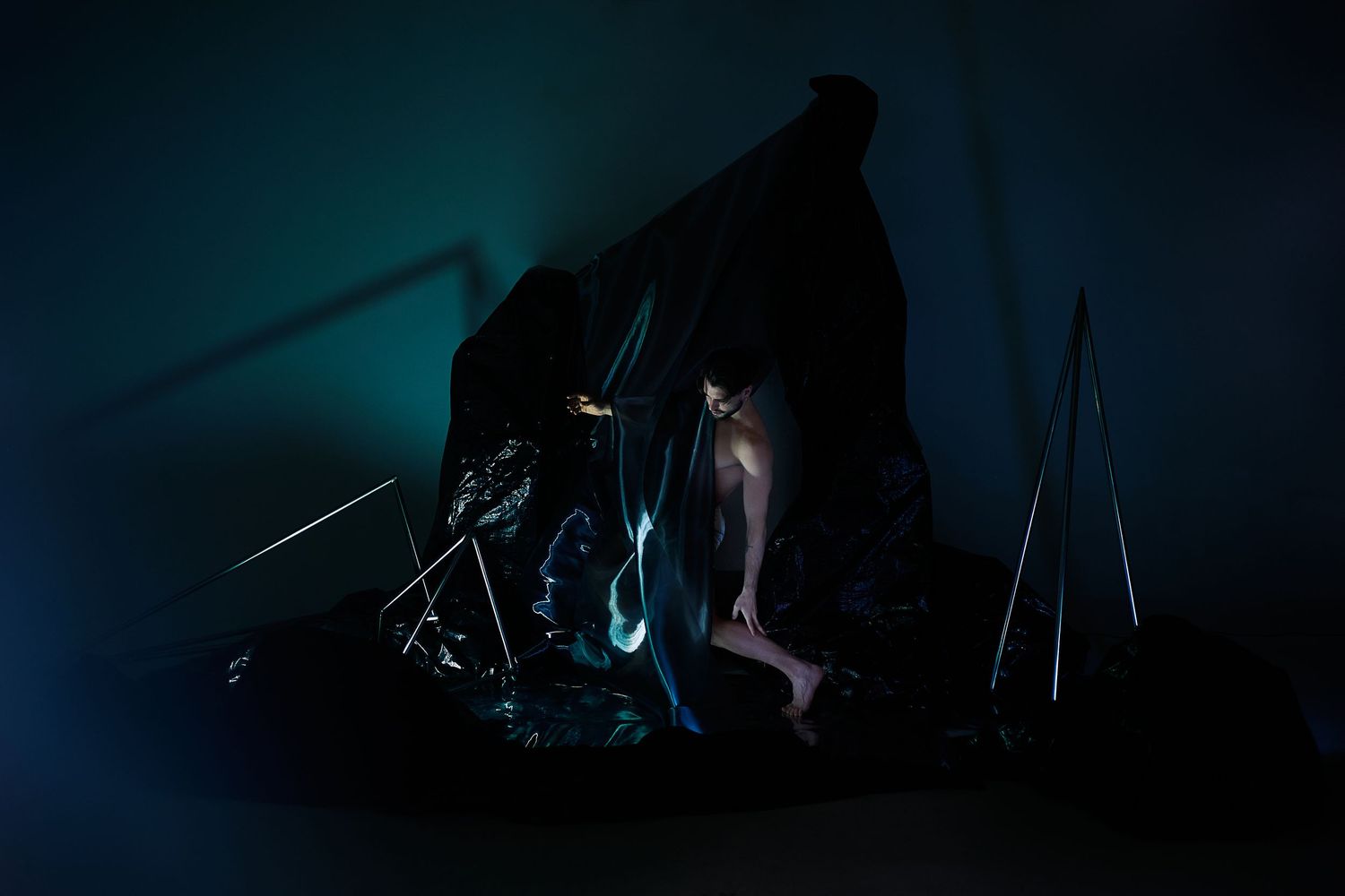 A mysterious dark silhouette illuminated by blue lights in a shadowy artistic performance or installation piece.
