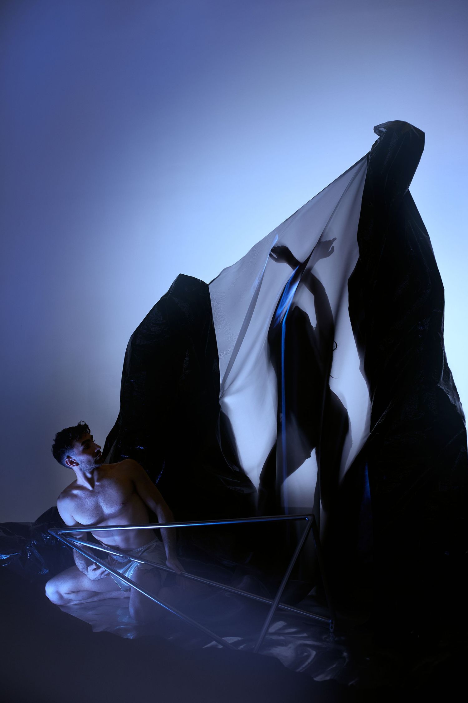 Dark silhouette figures loom over a dramatic scene with blue lighting and ethereal fabric creating an atmospheric composition.