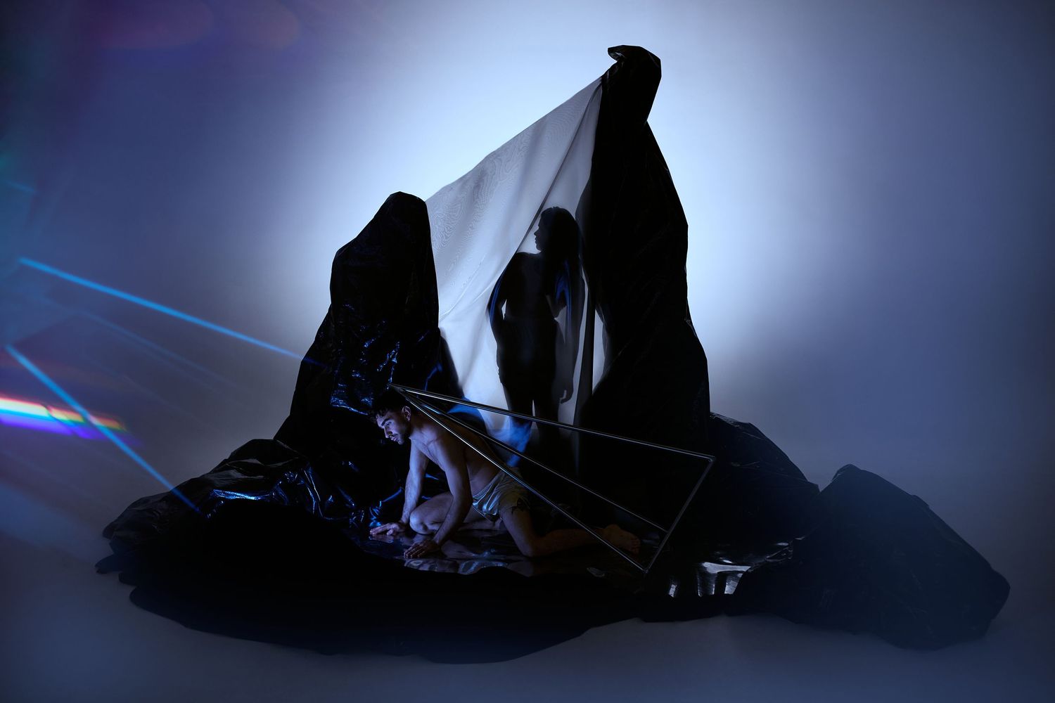 Dark silhouettes of ballet dancers performing against dramatic blue backlighting in a contemporary dance piece.