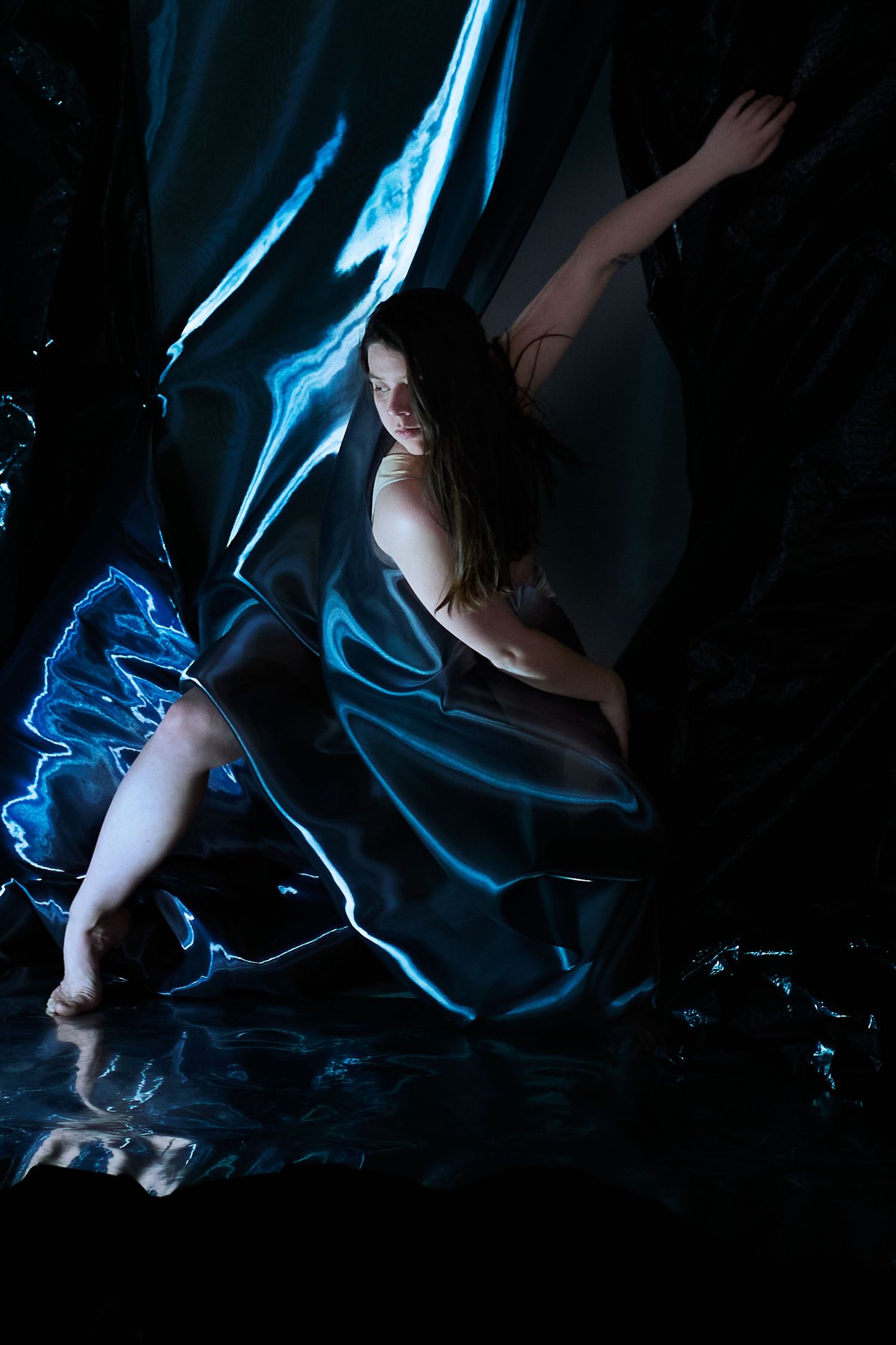 Artistic dark photography series showing silhouettes draped in flowing blue fabric against black background in ethereal poses.