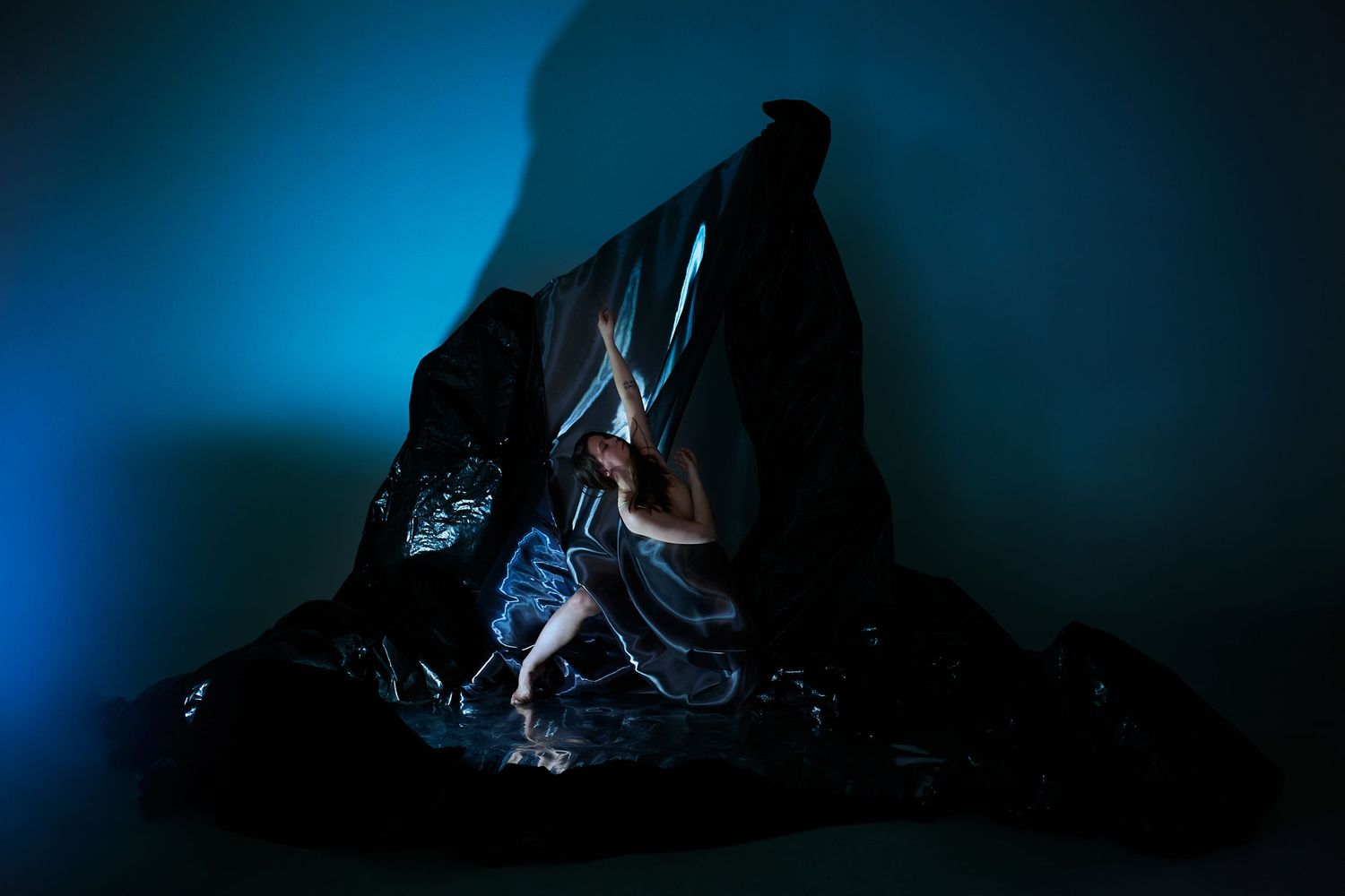 A silhouetted climbing figure scales a dark mountain peak against a dramatic blue backlit atmosphere.