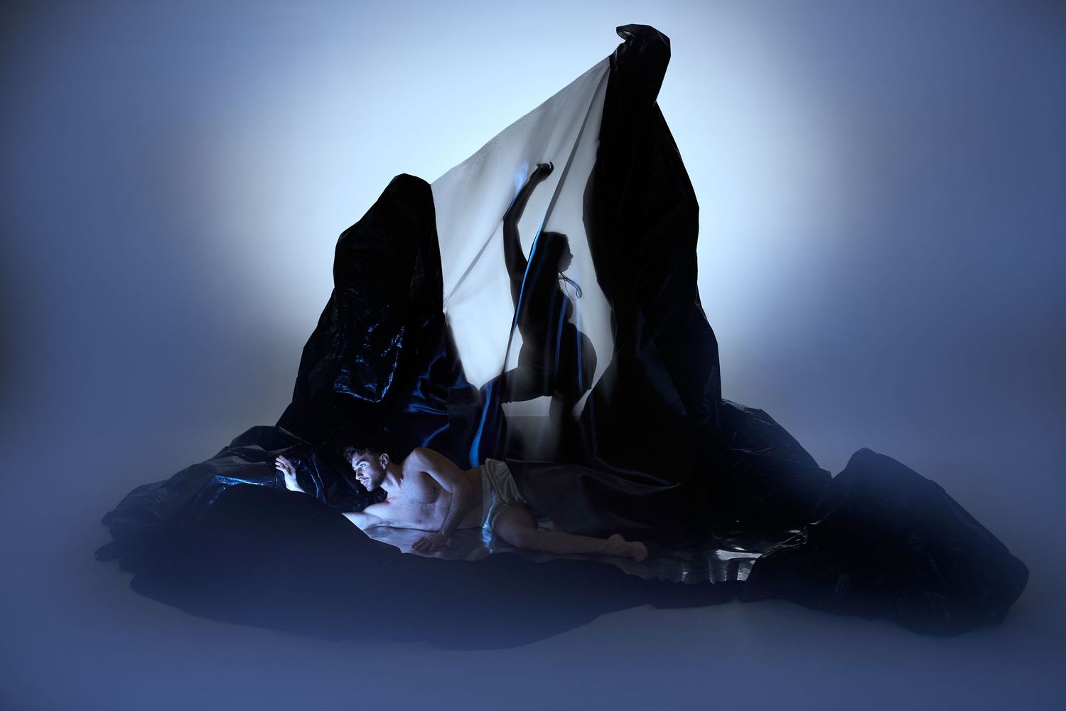 Silhouette of a dancer performing between dramatic rock formations with blue atmospheric lighting.