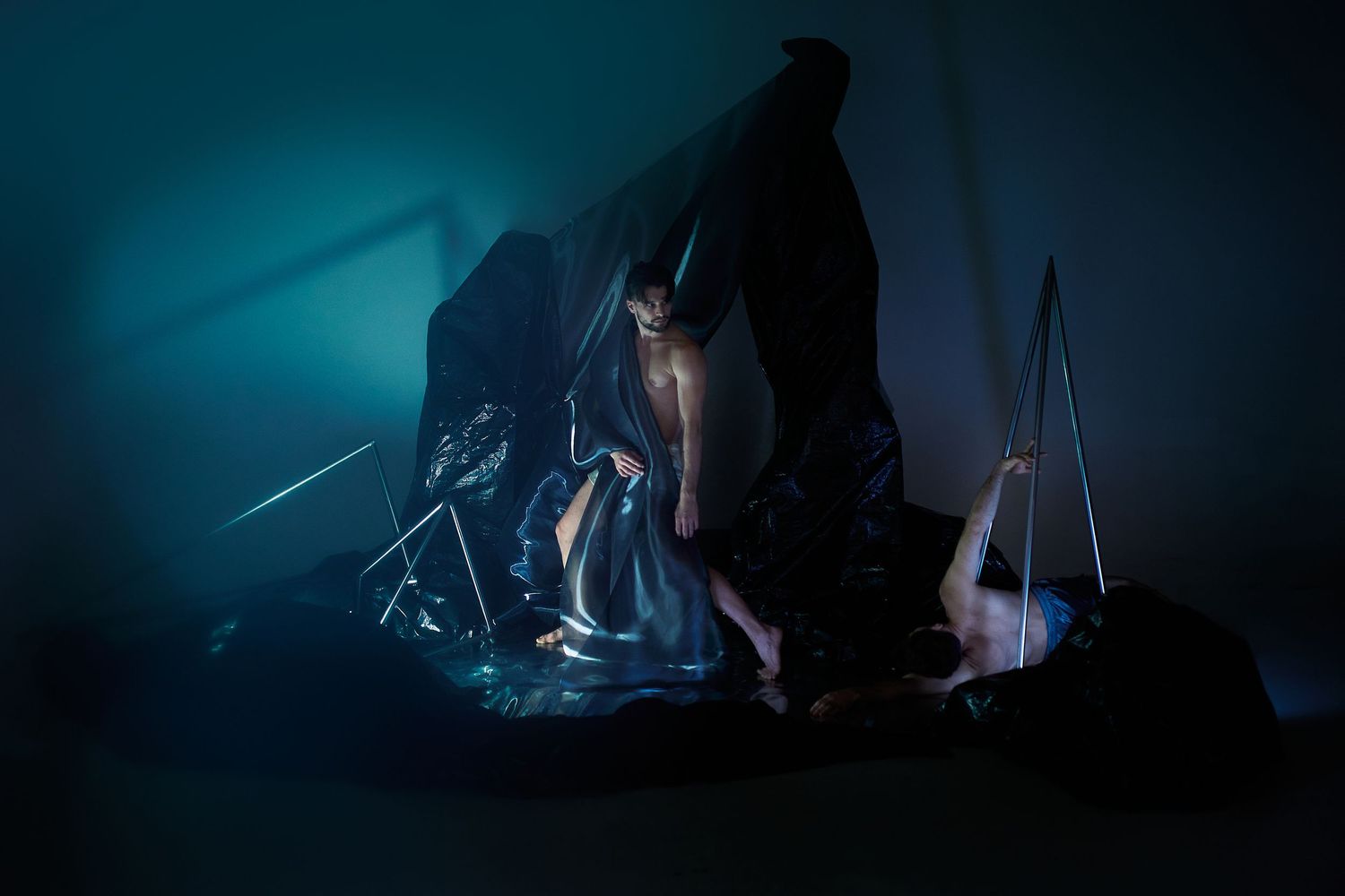 Mysterious figure in dark robe surrounded by ethereal blue lighting and sailing equipment creates dramatic silhouette.