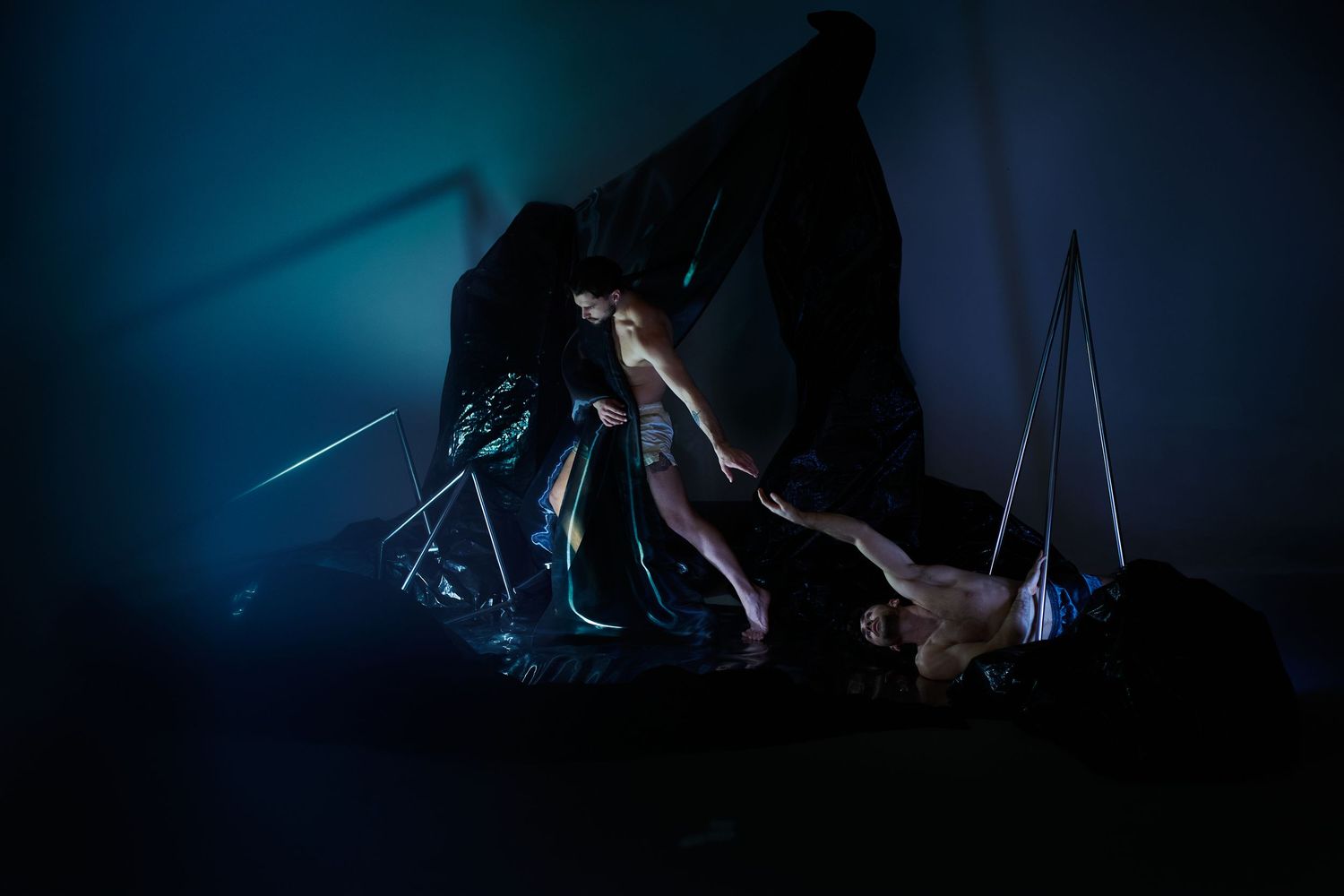 Dark silhouetted acrobats perform on aerial equipment against a moody blue backdrop during a circus performance.