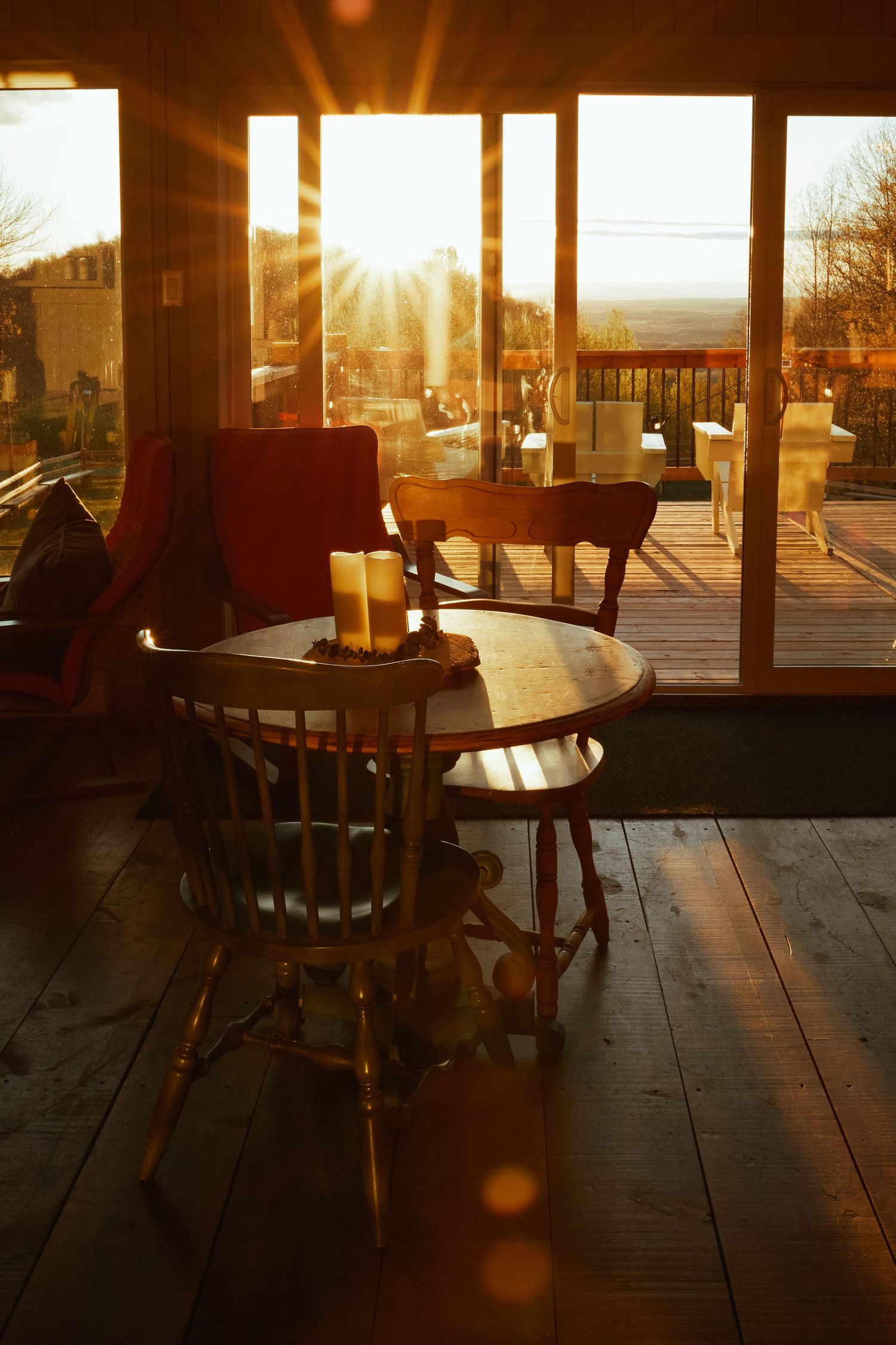 Sunlit wooden porch with empty tables and chairs at golden hour creating a warm, cozy restaurant atmosphere.