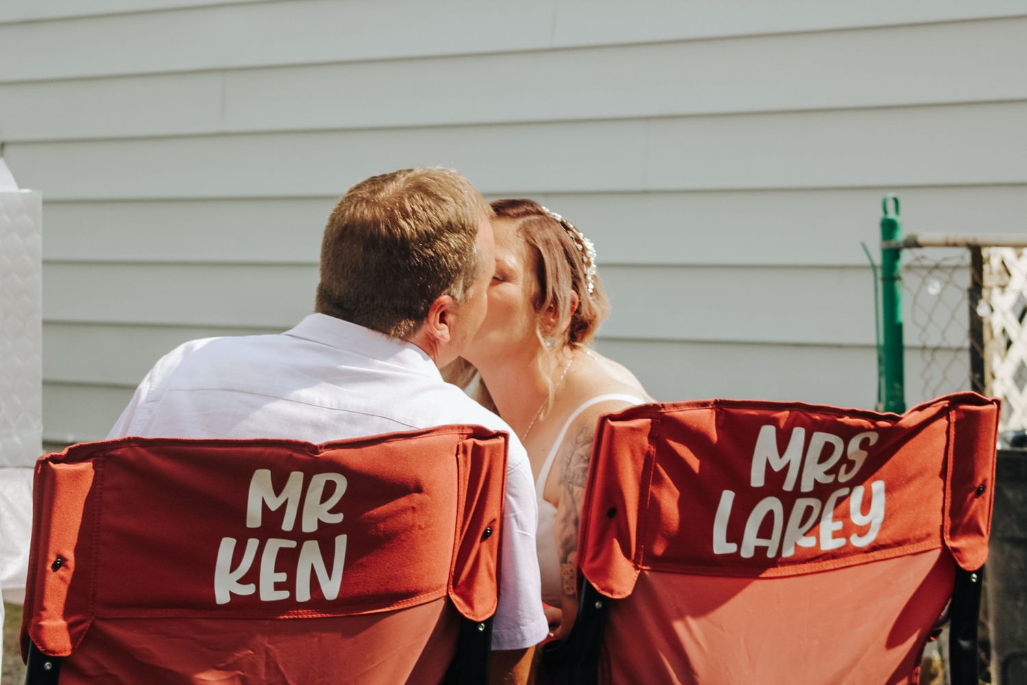 A couple sharing a kiss while sitting in red directors chairs labeled Mr. Len and Mrs. Loren.