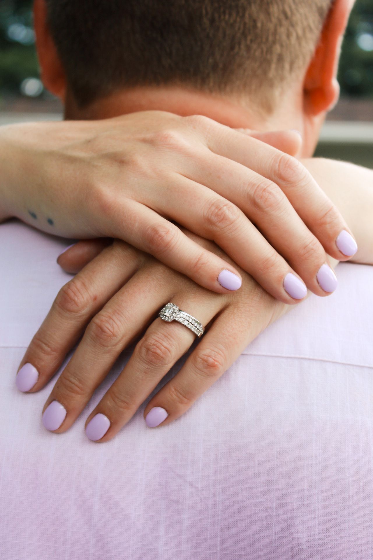 Close-up of manicured hands with engagement ring resting on shoulders.